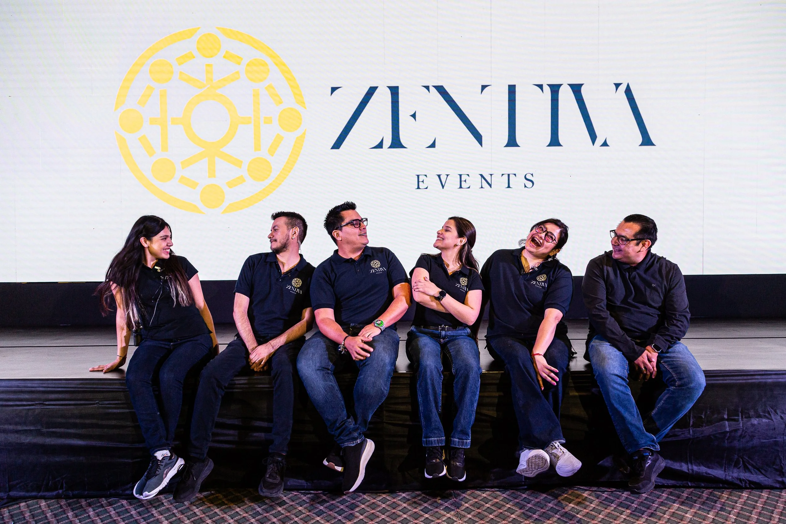 Personas sentadas en una banca en un evento de Zentiva Events, con un fondo que muestra el logotipo y el nombre del evento.