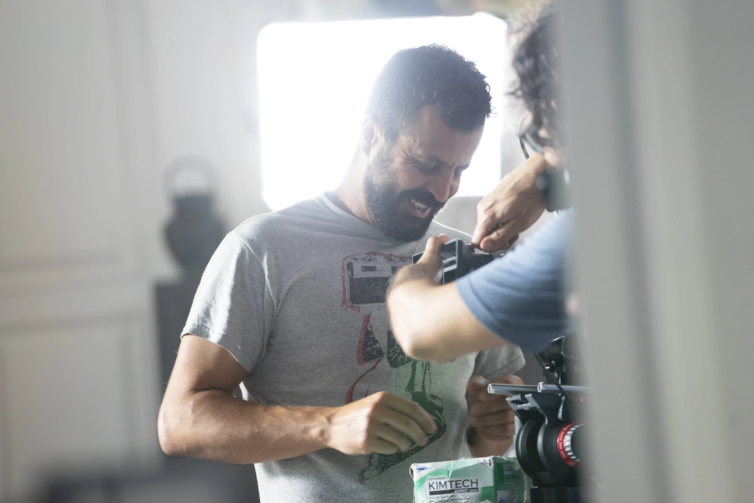Two men working together with a camera, one is adjusting the camera lens while the other is helping, in a well-lit room.