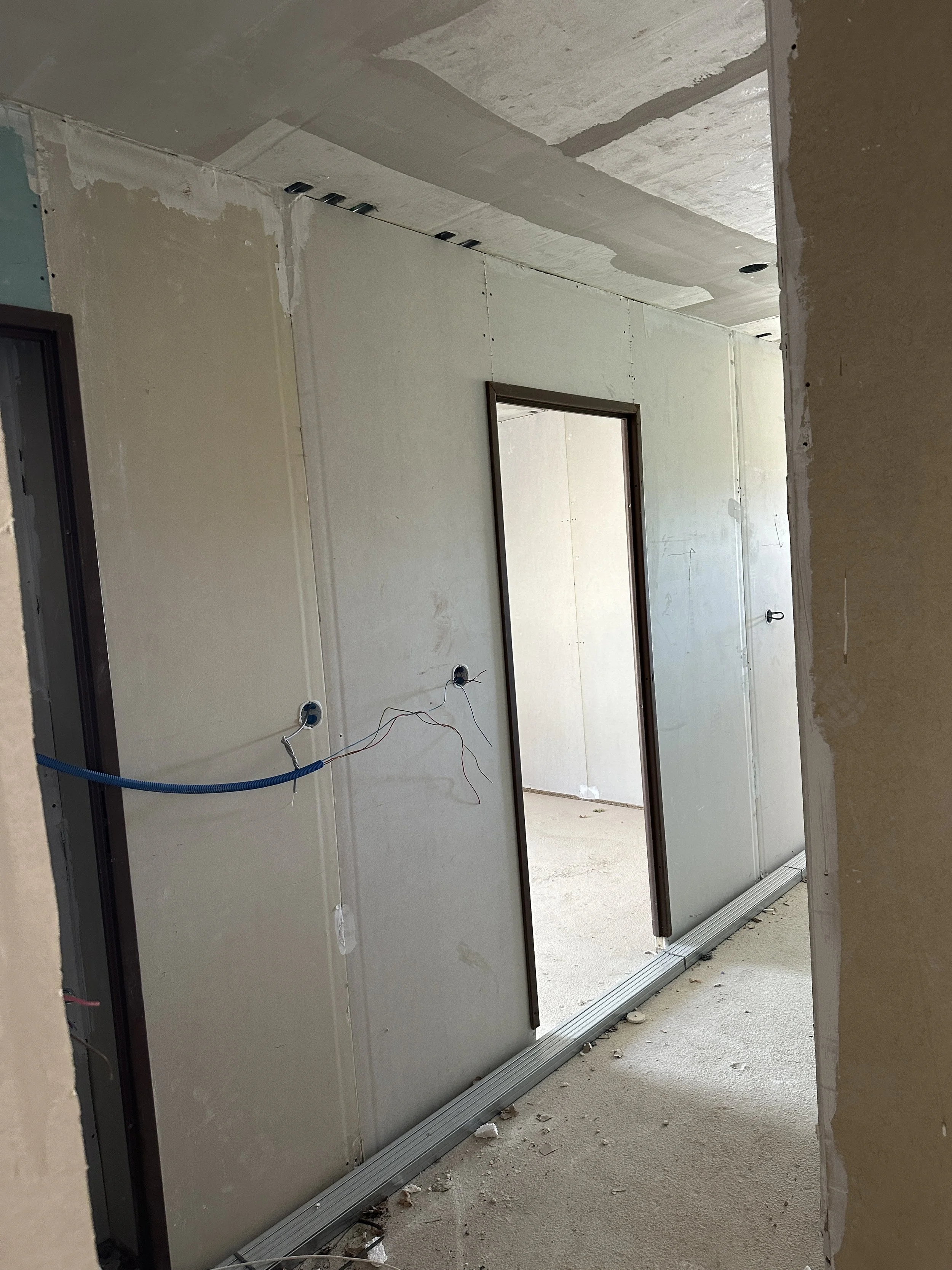 Un mur en construction avec un cadre de porte, une partie du plafond en travaux avec des câbles électriques et des trous, proposition d'installation électrique en cours.