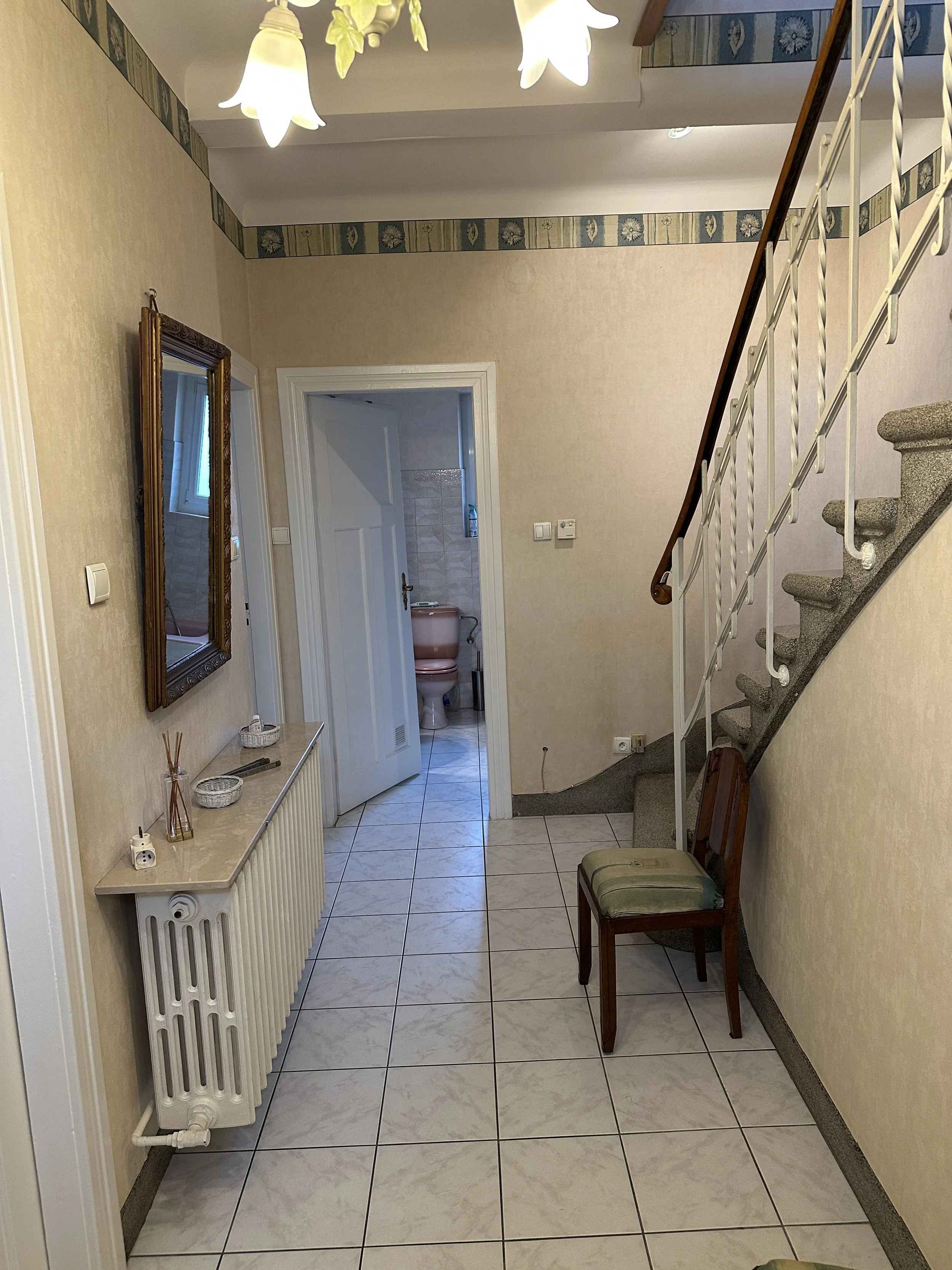 État avant travaux – entrée maison de maître avec papier peint fleuri années 80, carrelage gris, escalier granit et radiateur fonte – avant rénovation complète par Anthony Mambré Design, architecte d'intérieur