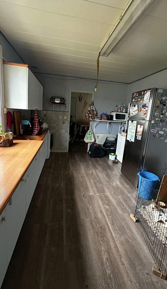 Cuisine avec plan de travail en bois, réfrigérateur noir couvert de magnets, micro-ondes, garde-manger, panier à linge et un animal de compagnie dans une cage.