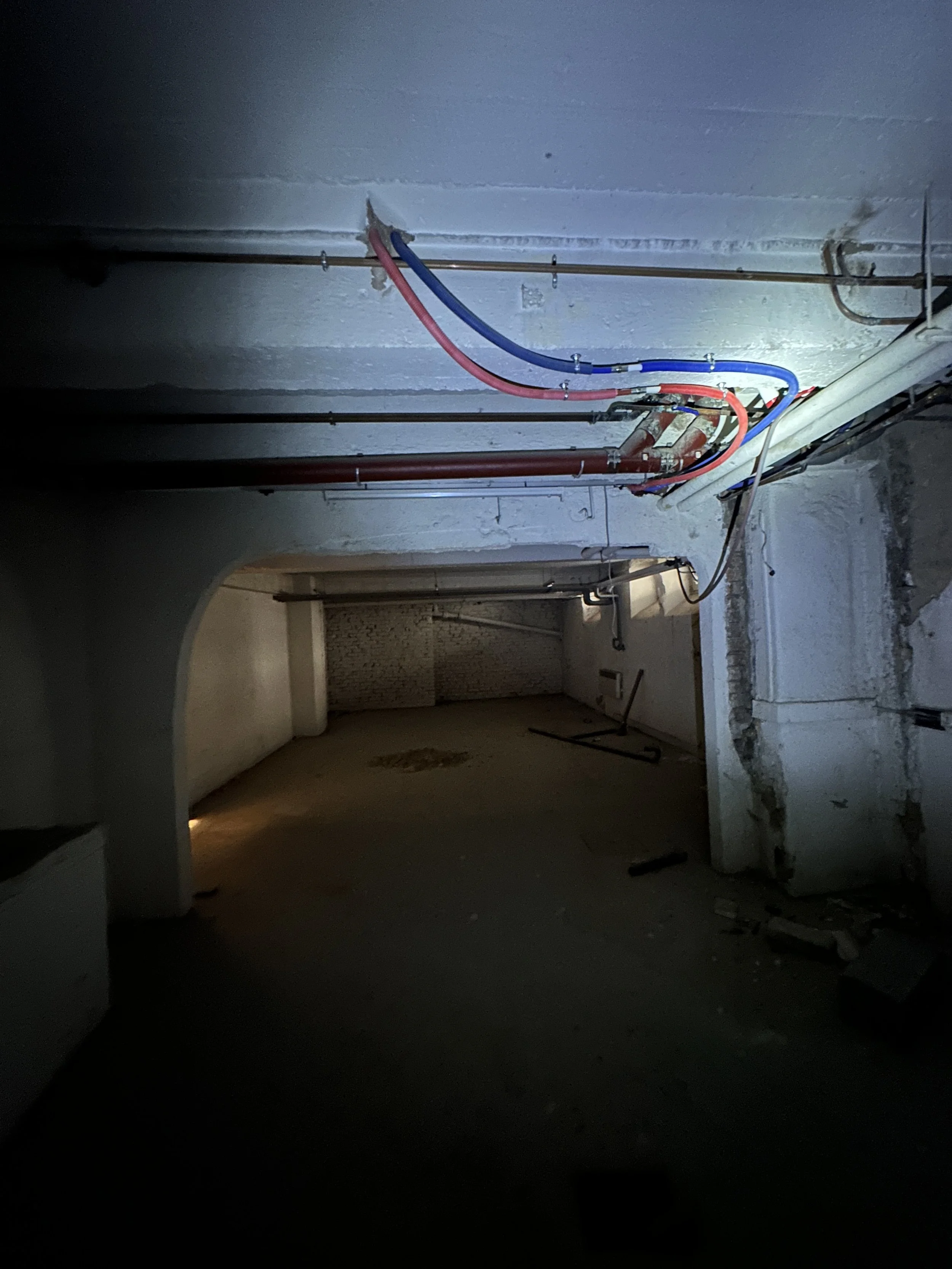 Installation de conduites électriques dans un espace en travaux, avec tuyaux rouges, bleus et blancs fixés au plafond.