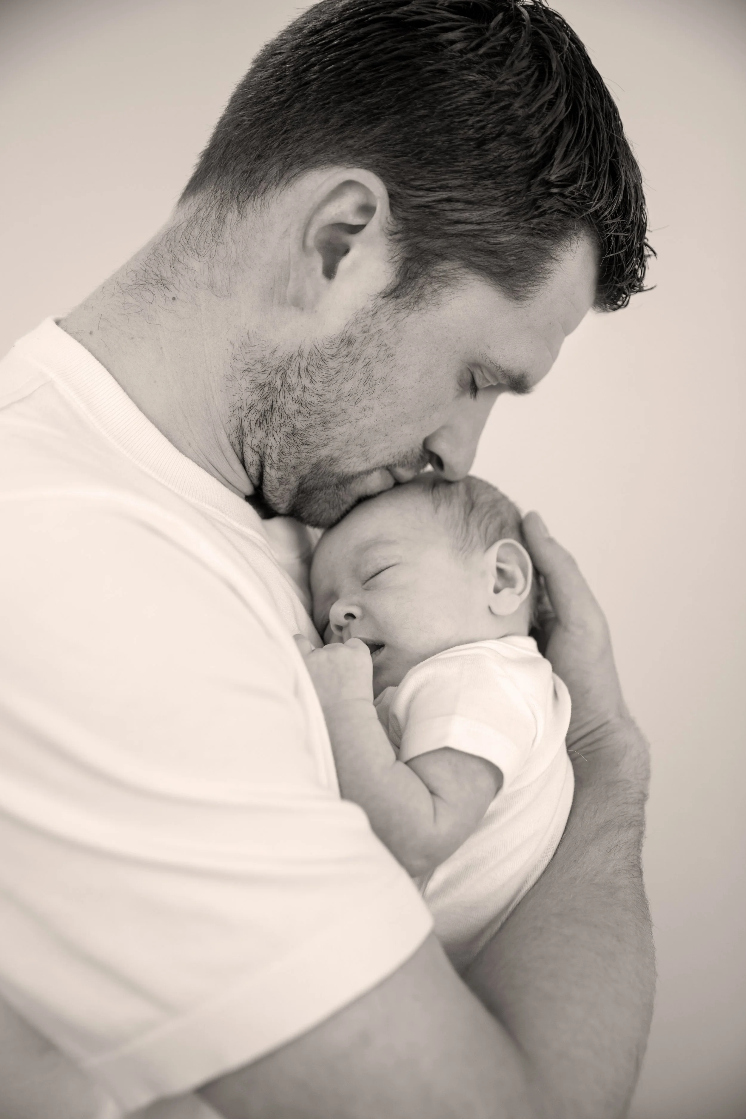 A man holds a sleeping newborn baby close, touching foreheads in a tender moment.