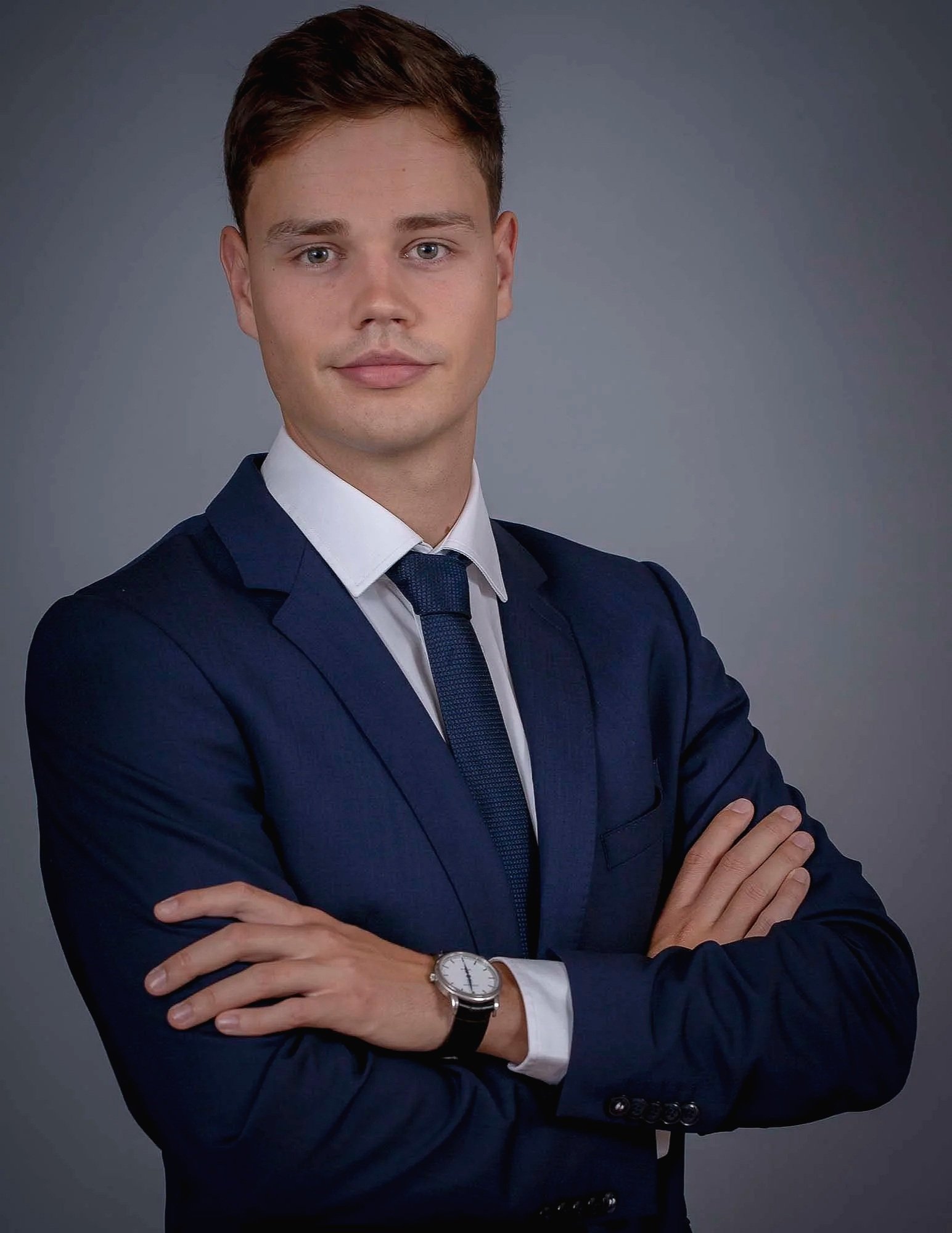 Zwei lachende Menschen, eine Frau und ein Mann, bei einer Veranstaltung. Sie stehen an einem Tisch mit einer Vase mit Blumen und einem schwarzen Etui. Im Hintergrund sind weitere Personen und ein Fenster mit Vorhängen zu sehen.