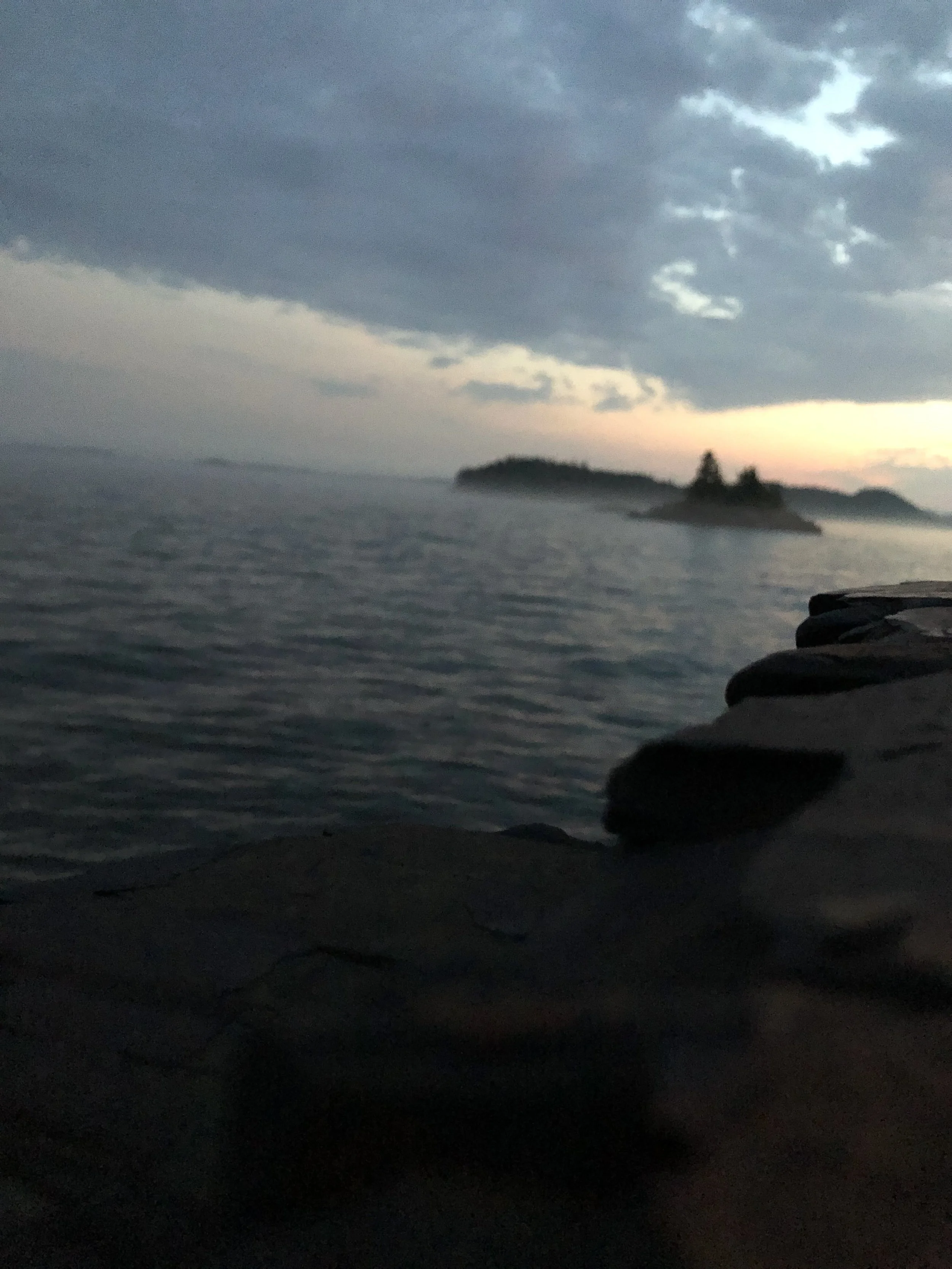 Dark, cloudy evening over a calm body of water with a small island in the distance and stacked rocks in the foreground.