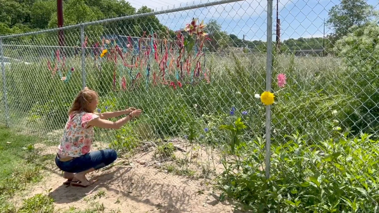 Kristie Beth Ihde anchoring flowers to the fence, shaping meaning through simple gestures.