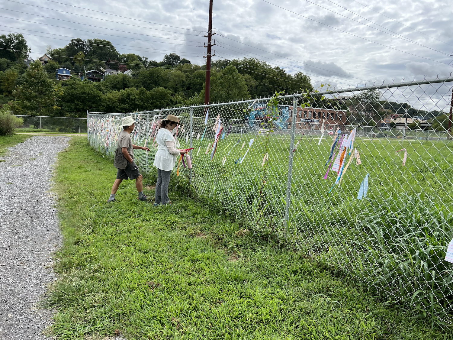 Visitors attaching fabric strips to The Ties That Bind Asheville installation along a fence in Asheville, North Carolina.