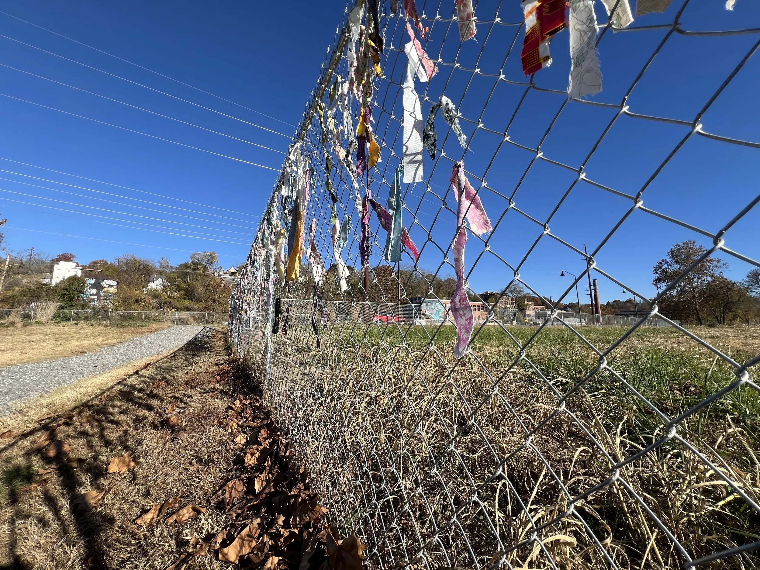 Fence shadows and fallen leaves gather along the riverside edge of the installation.