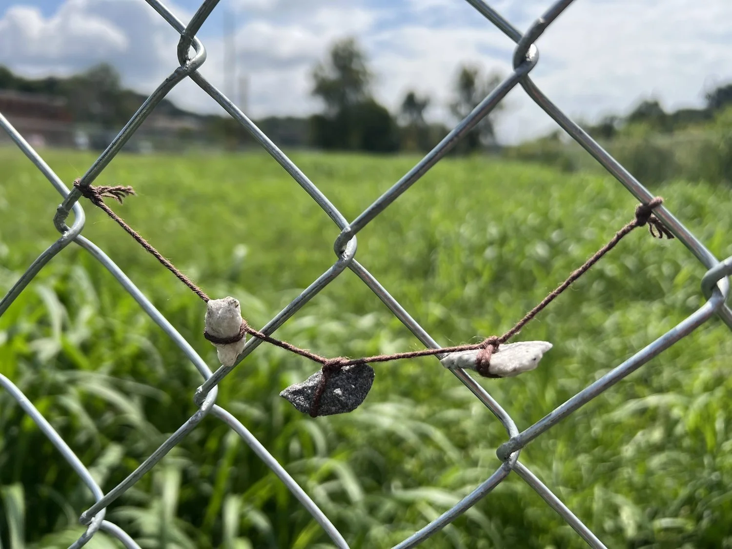 A piece of twine and gravel from the path — someone has crafted a small piece of jewelry and left it on the fence.