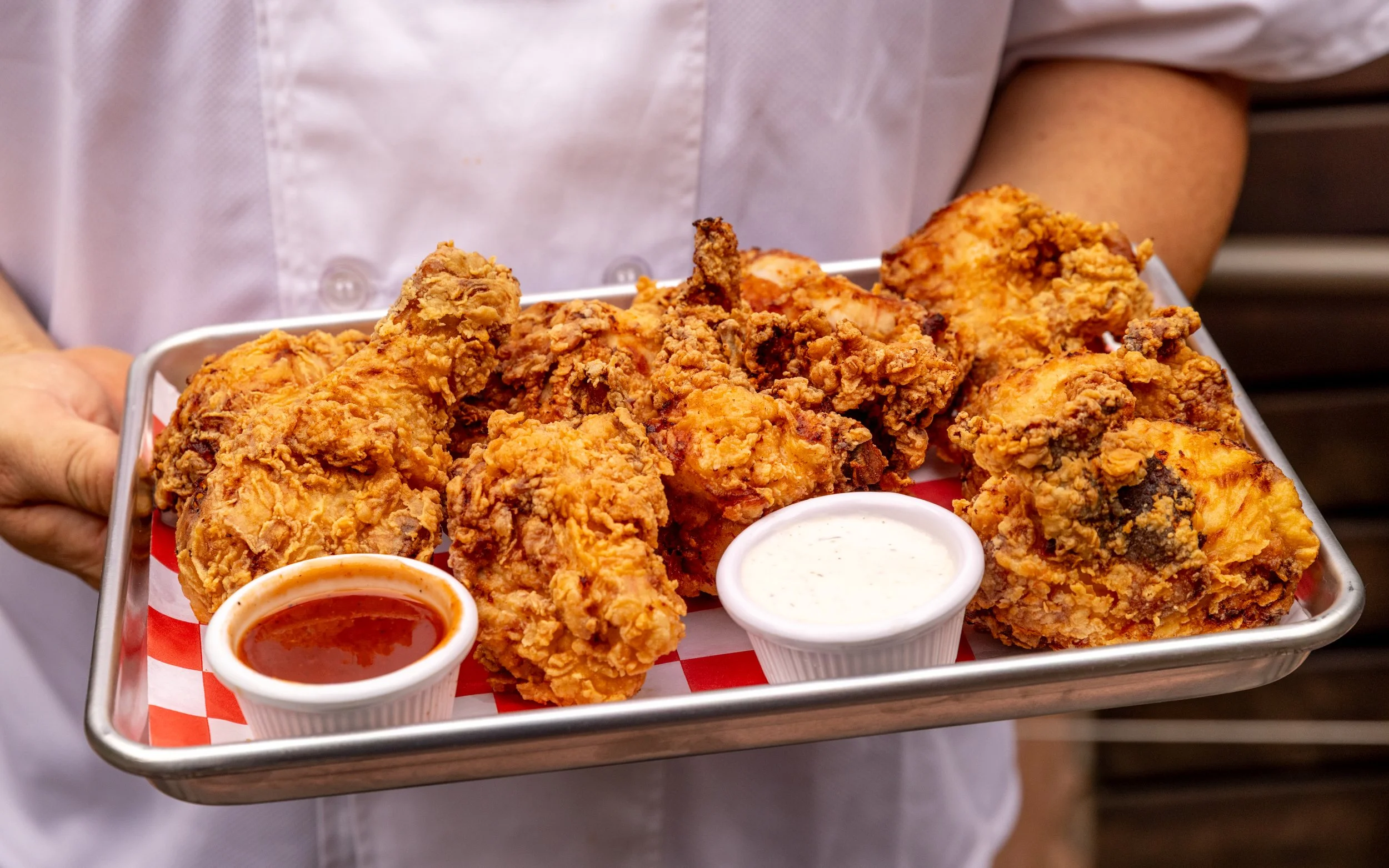 Baked chicken with roasted potatoes, dipping sauce, and yellow plastic utensils on a checkered paper-lined tray.