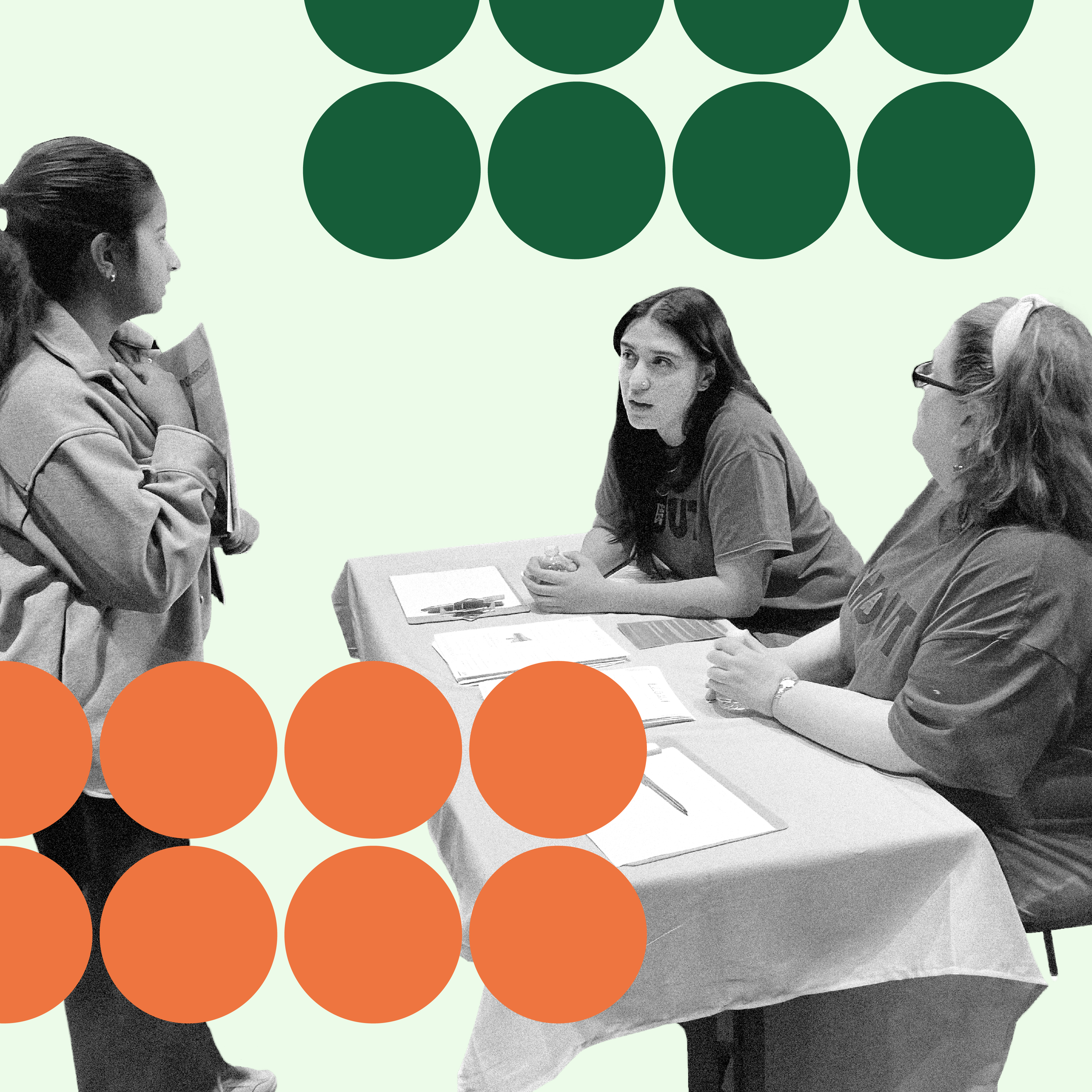 Two organizers wearing SHOUT t-shirts sit at a large table with papers, speaking with a standing person holding papers. Two sets of two rows of decorative arrows above and below them in dark green and orange.