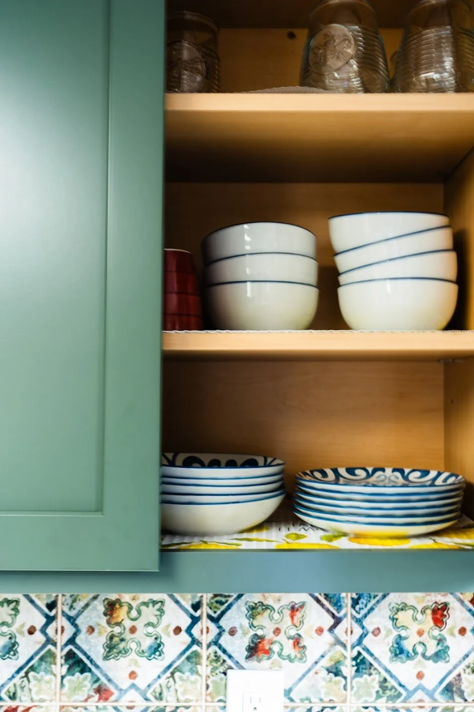 Kitchen cabinet with pottery bowls and glasses, tiled backsplash, electrical outlet.