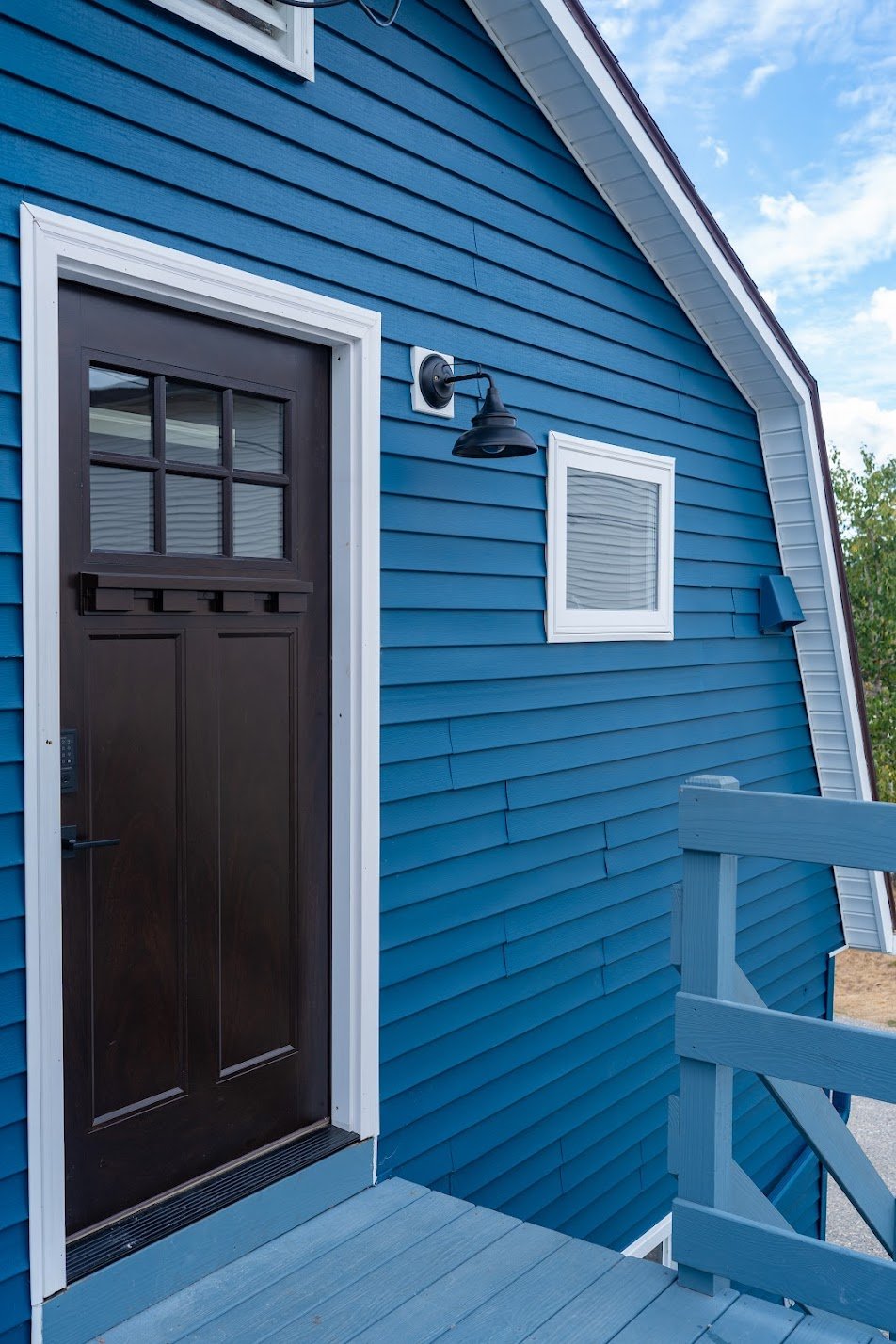 Blue house exterior with black front door, white trim, small window with blinds, black outdoor light fixture, and wooden staircase with white railing.
