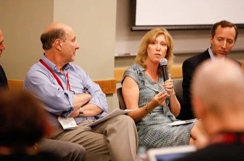 Victoria Maizes answering a question during a panel discussion, with two men seated beside her and an audience in front.