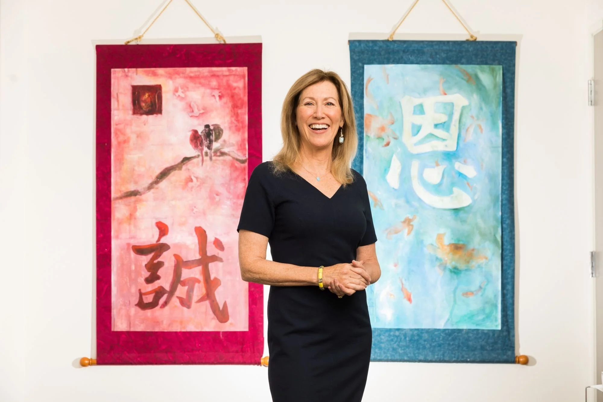 Dr. Victoria Maizes presenting at an integrative medicine conference  wearing a black dress and standing in front of two hanging pieces of artwork with Chinese characters.