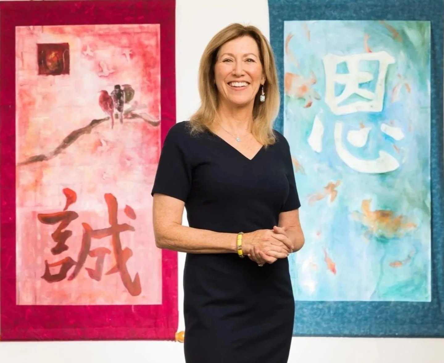 Integrative Medicine doctor, Victoria Maizes, standing in front of two pieces of artwork with Chinese characters, one with a red background and one with a blue background.