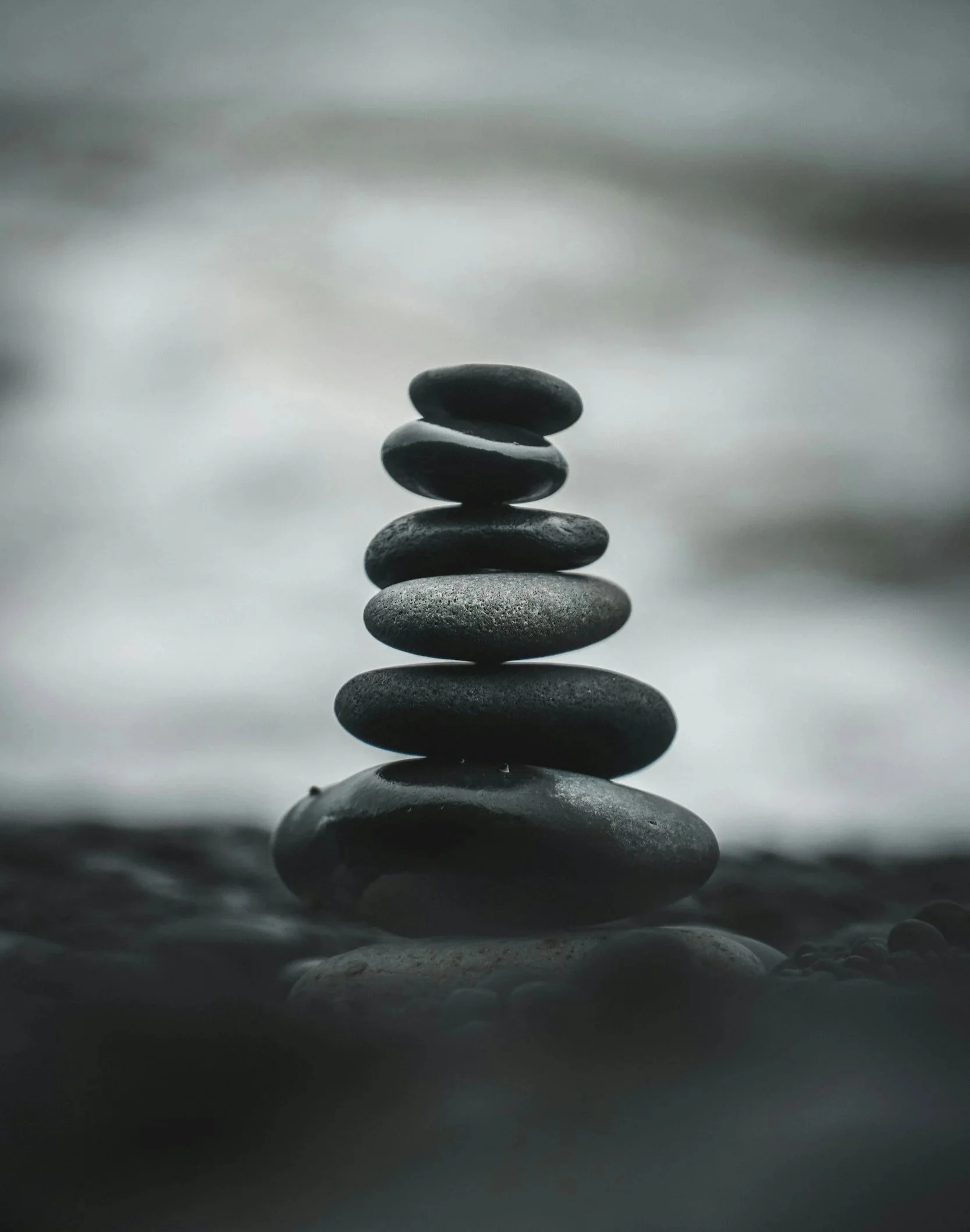 Stacked smooth black stones balanced on top of each other on a flat surface, with a blurred background.