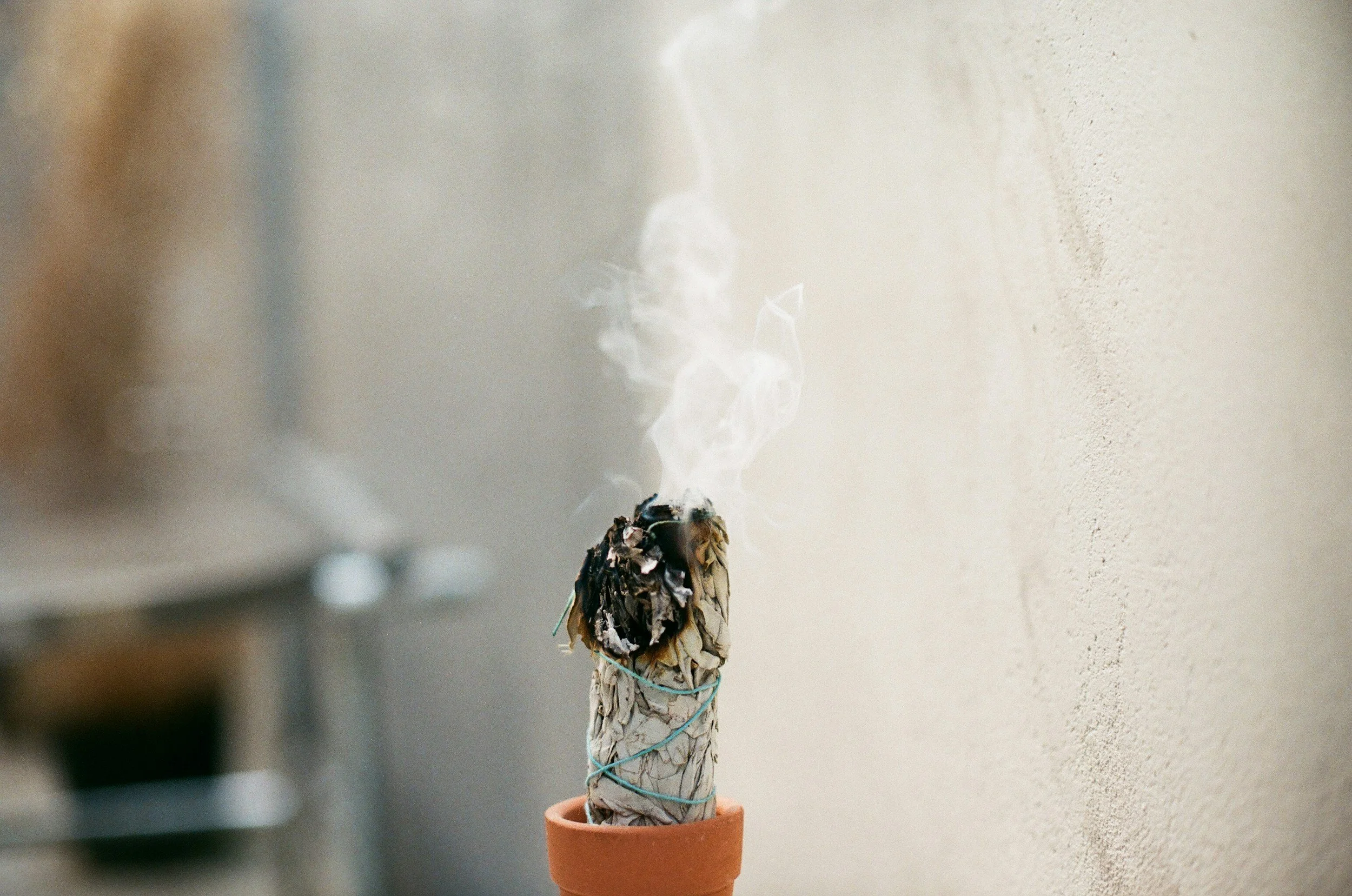 Smoke rising from a burning sage bundle in a terracotta pot