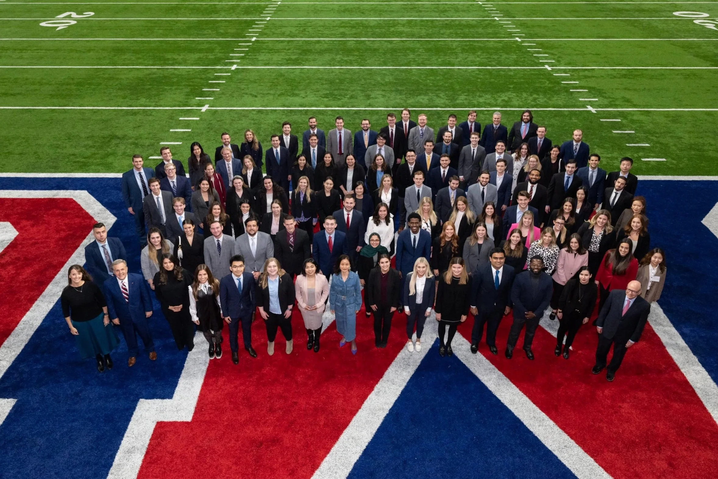 A large group of diverse people in business attire standing on a football field, forming a semi-circle for a group photo.