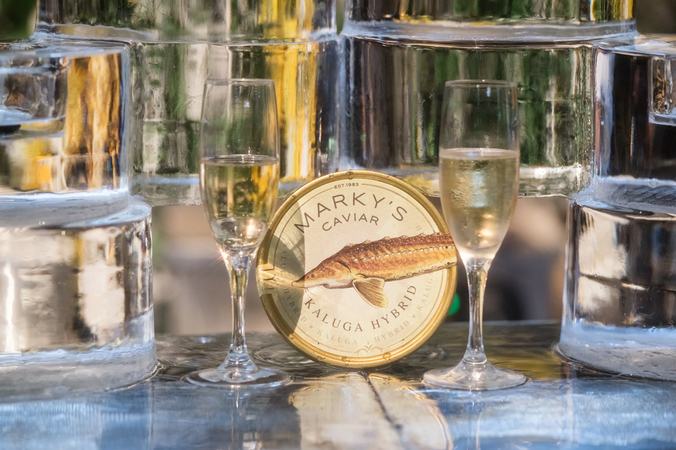 A can of Marky's Caviar Kaluga Hybrid, two glasses of champagne, and large ice blocks.