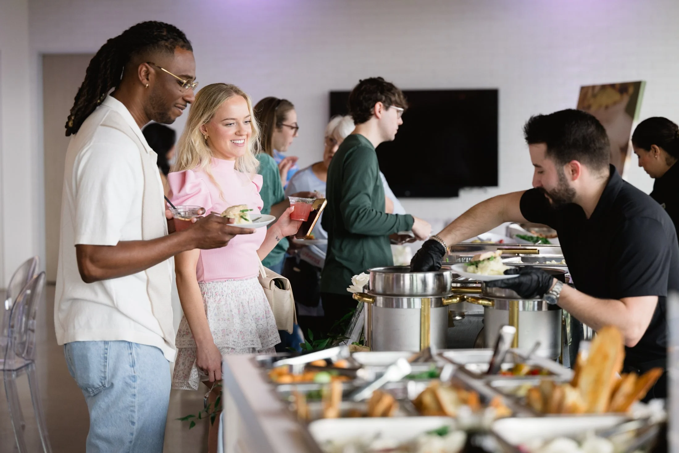 People standing in line at a food buffet, serving themselves food from chafing dishes.