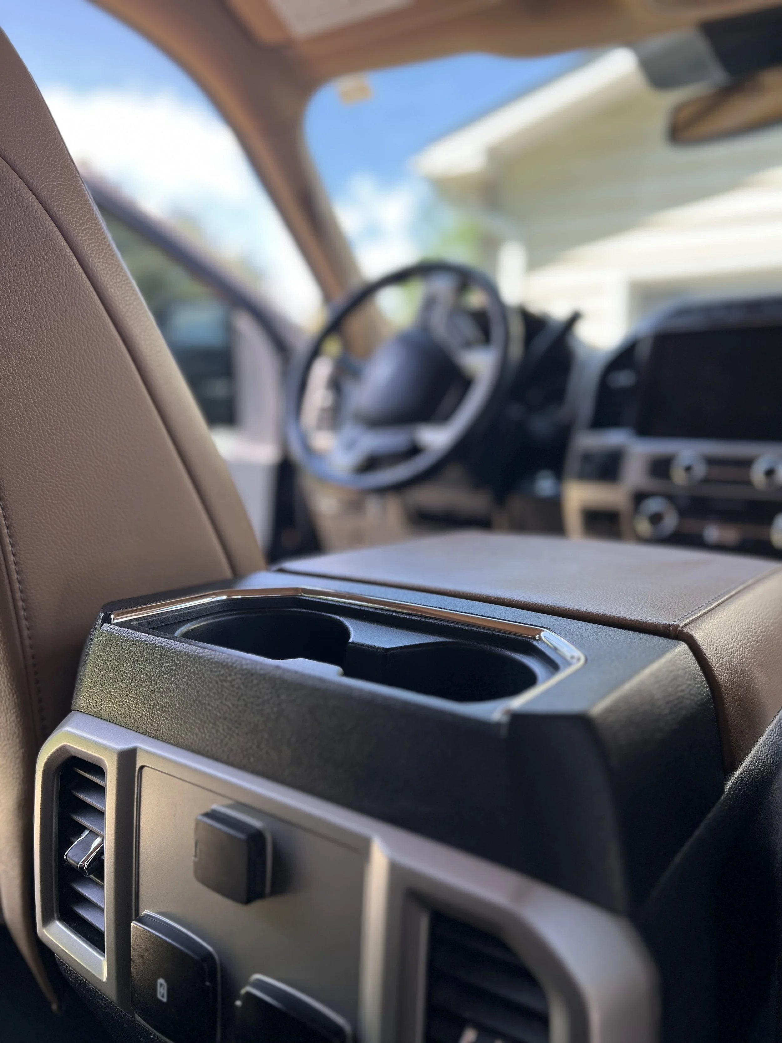 The interior view of a vehicle showing a beige seat, a dashboard with climate control vents and switches, and an open sunroof revealing blue sky outside.