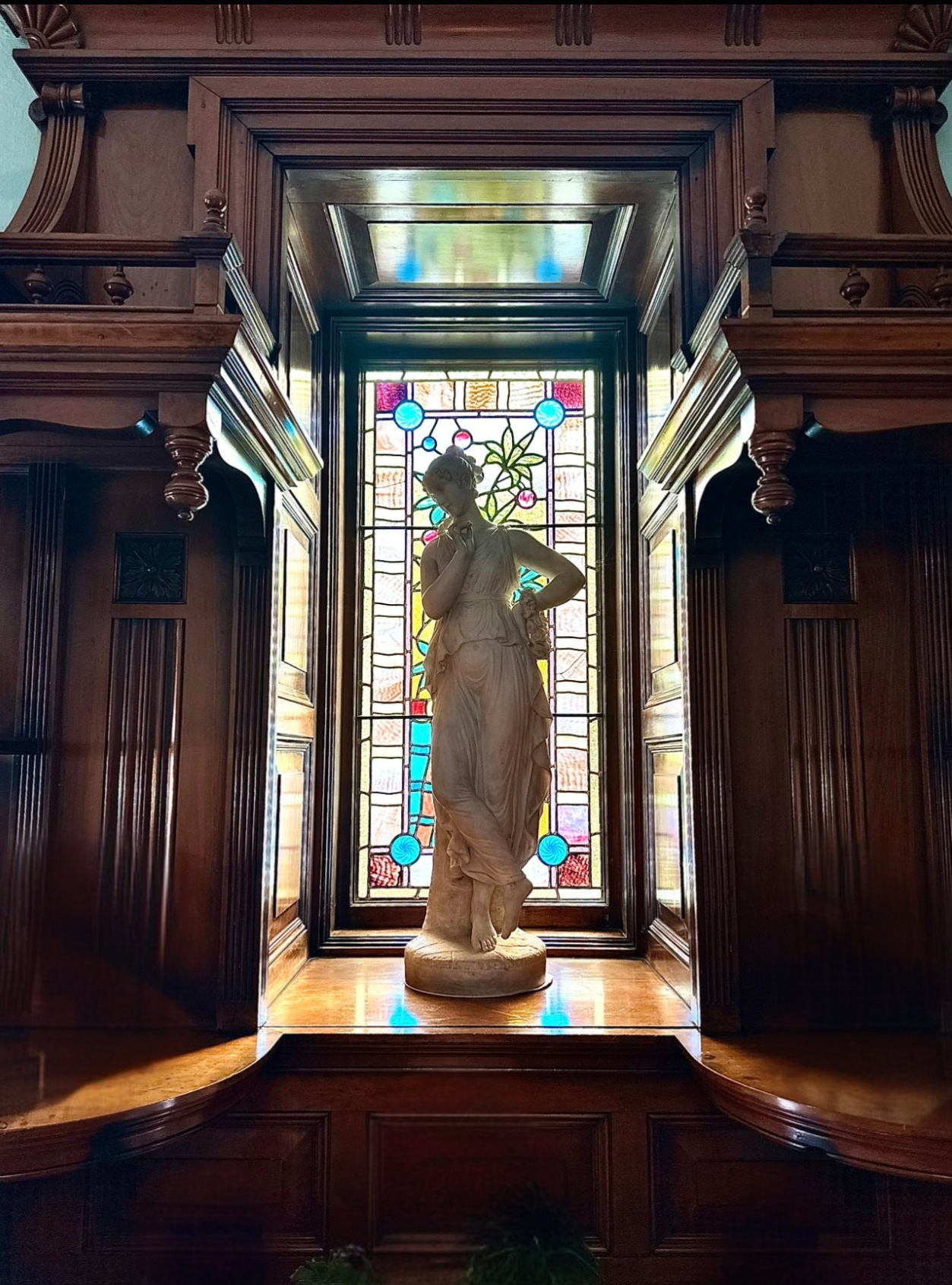 A marble statue of a woman in front of stained glass