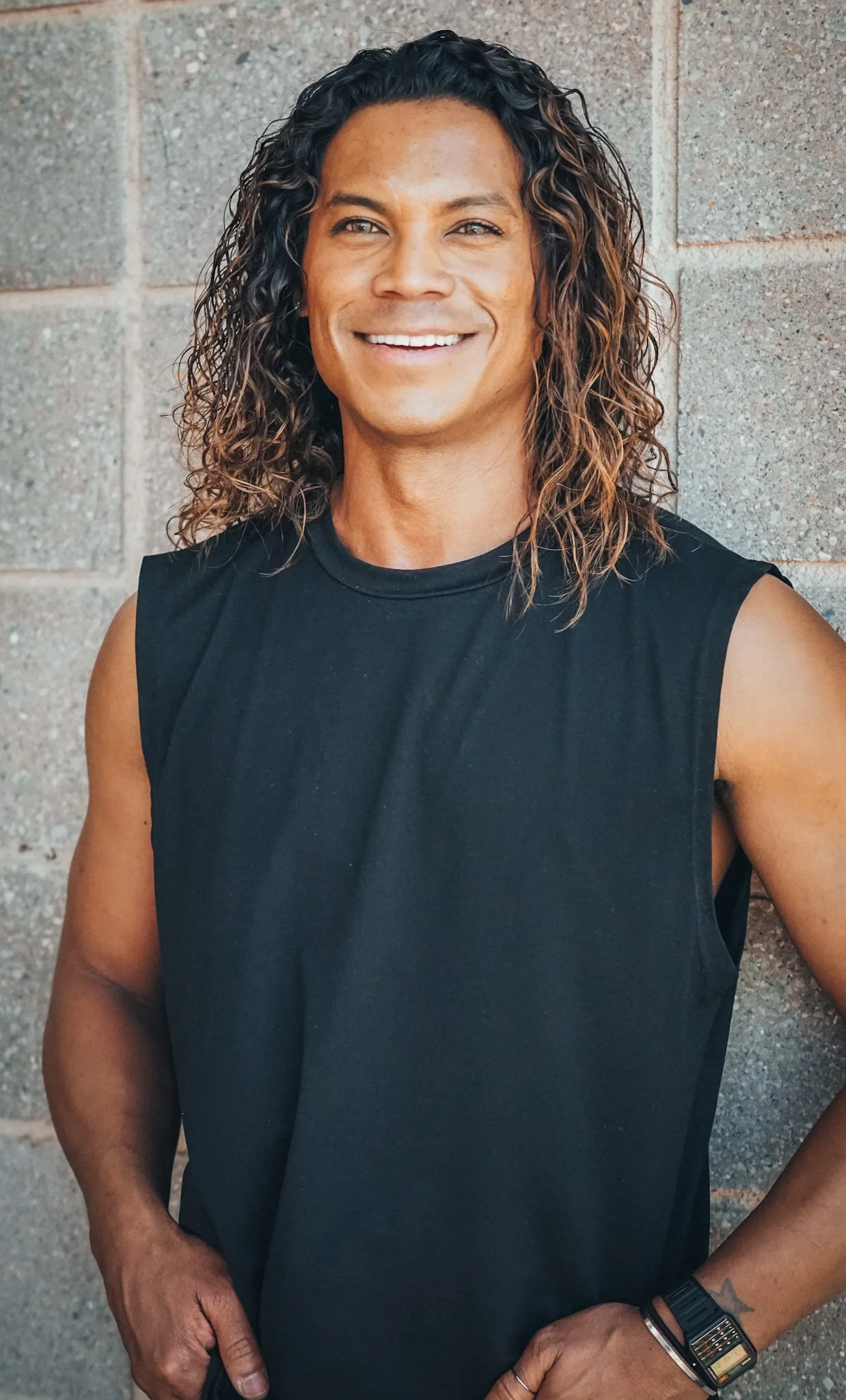 A man with curly dark hair smiling, wearing a black t-shirt, standing outdoors