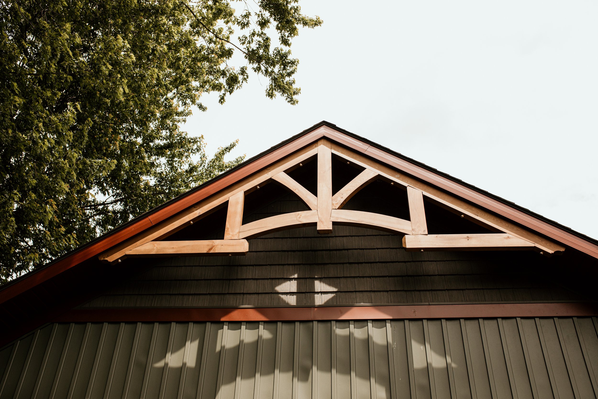 Close-up of a house's gabled roof with decorative wooden support beams, metal roofing, and a green siding wall.