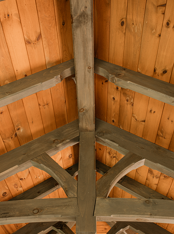 Looking up at a wooden ceiling and beam structure in a cabin or barn