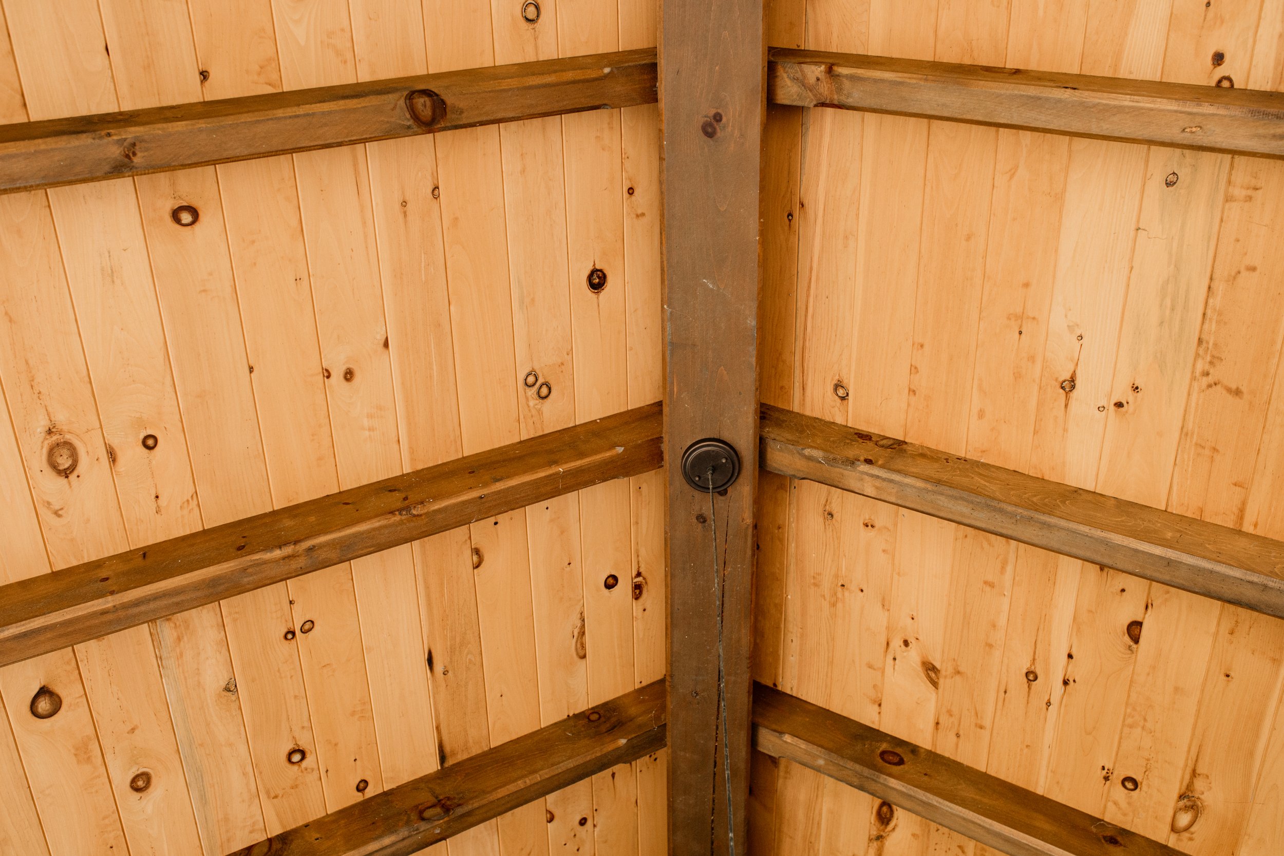 Wooden ceiling with visible beams and paneling, including a central metal support beam with a hanging pull switch.