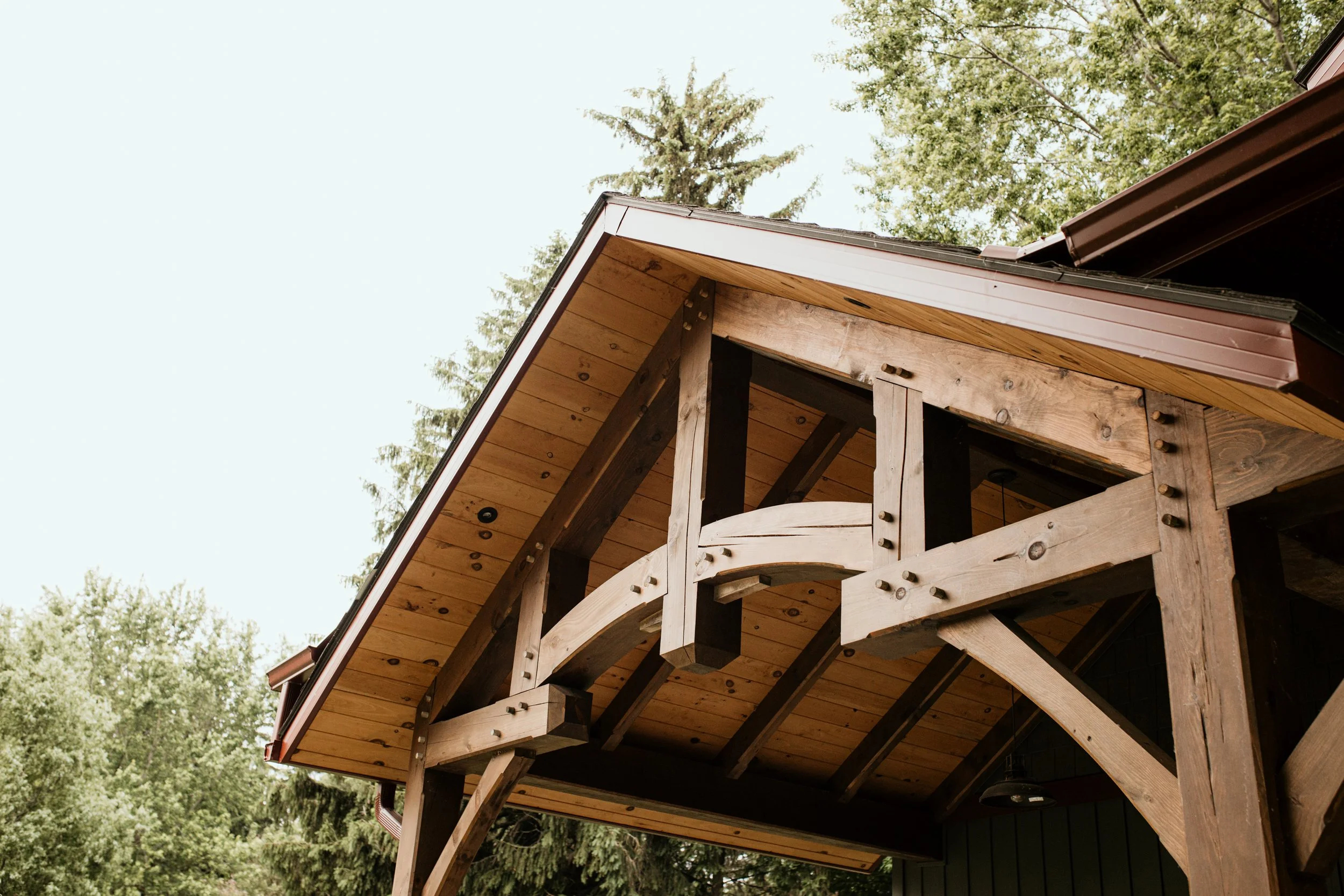 Close-up of a wooden house's porch with a decorative railing, an overhanging roof, surrounded by green trees.