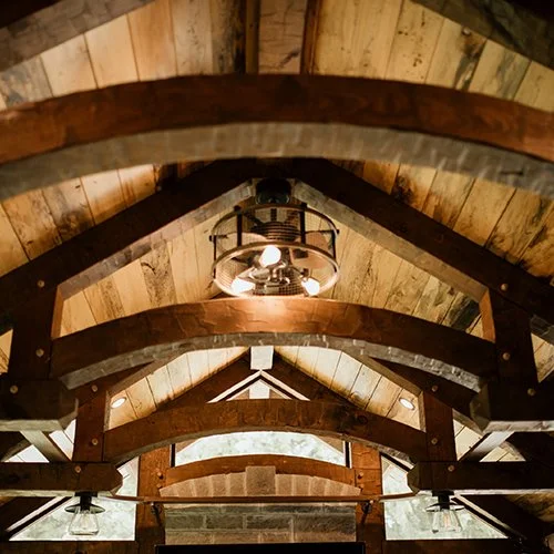 Ceiling of a rustic wooden barn with exposed beams and a central industrial-style lantern light fixture.