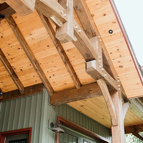 Wooden ceiling and support beams underneath a partially constructed or renovated outdoor porch or deck area with visible nails.