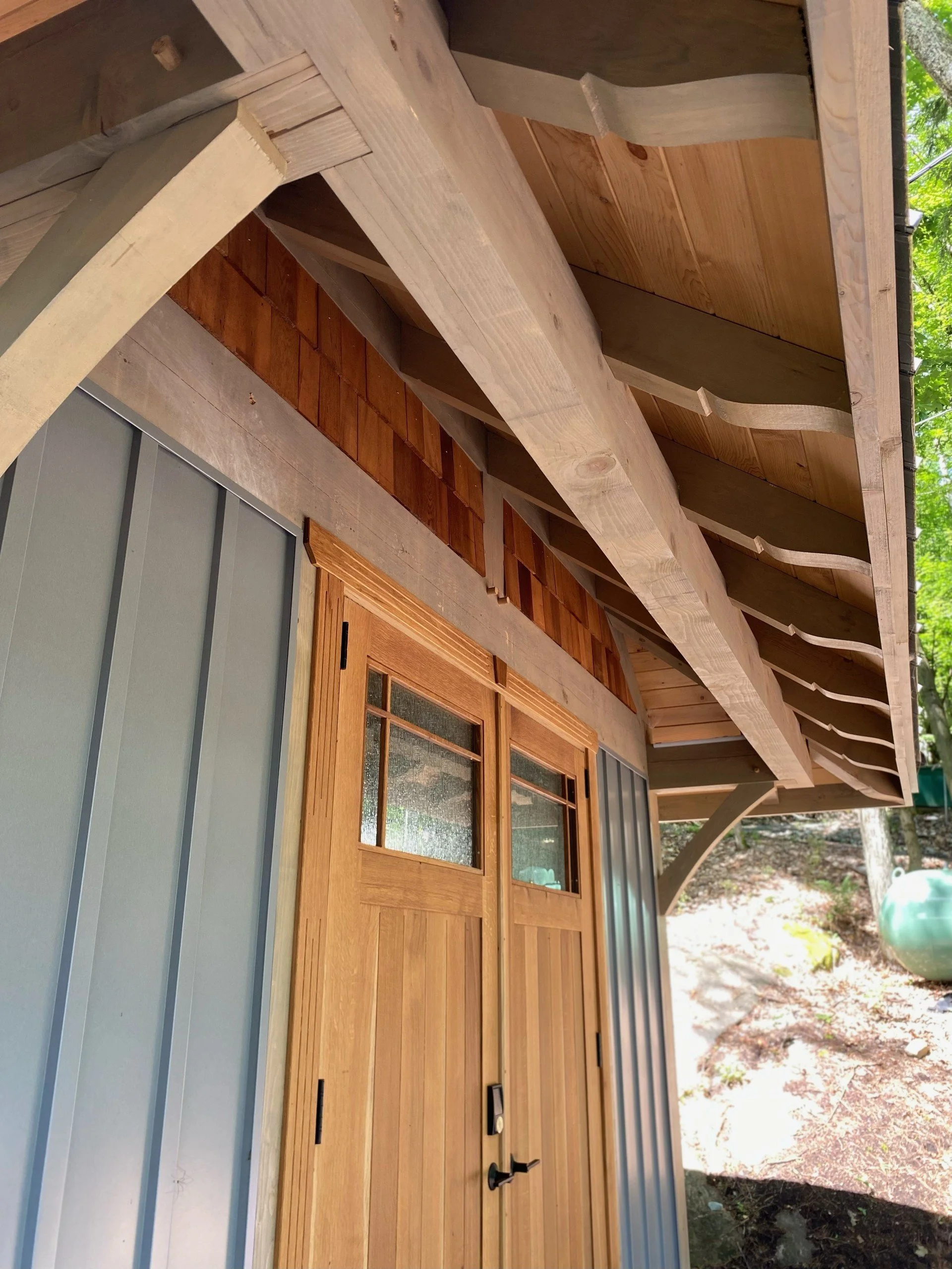 Close-up view of the underside of a wooden building’s roof with visible rafters, siding, and a wooden door.