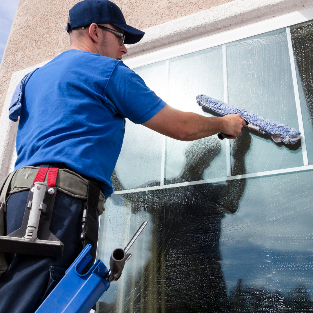Man cleaning a large glass window with a squeegee.