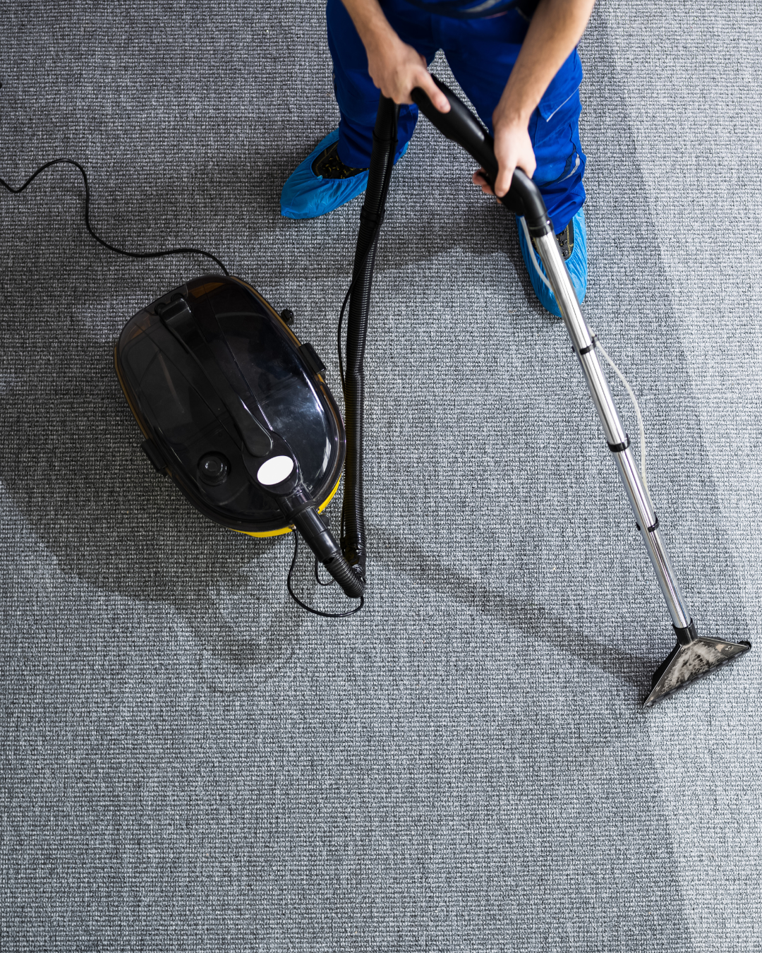 Person using a vacuum cleaner on a gray carpeted floor.