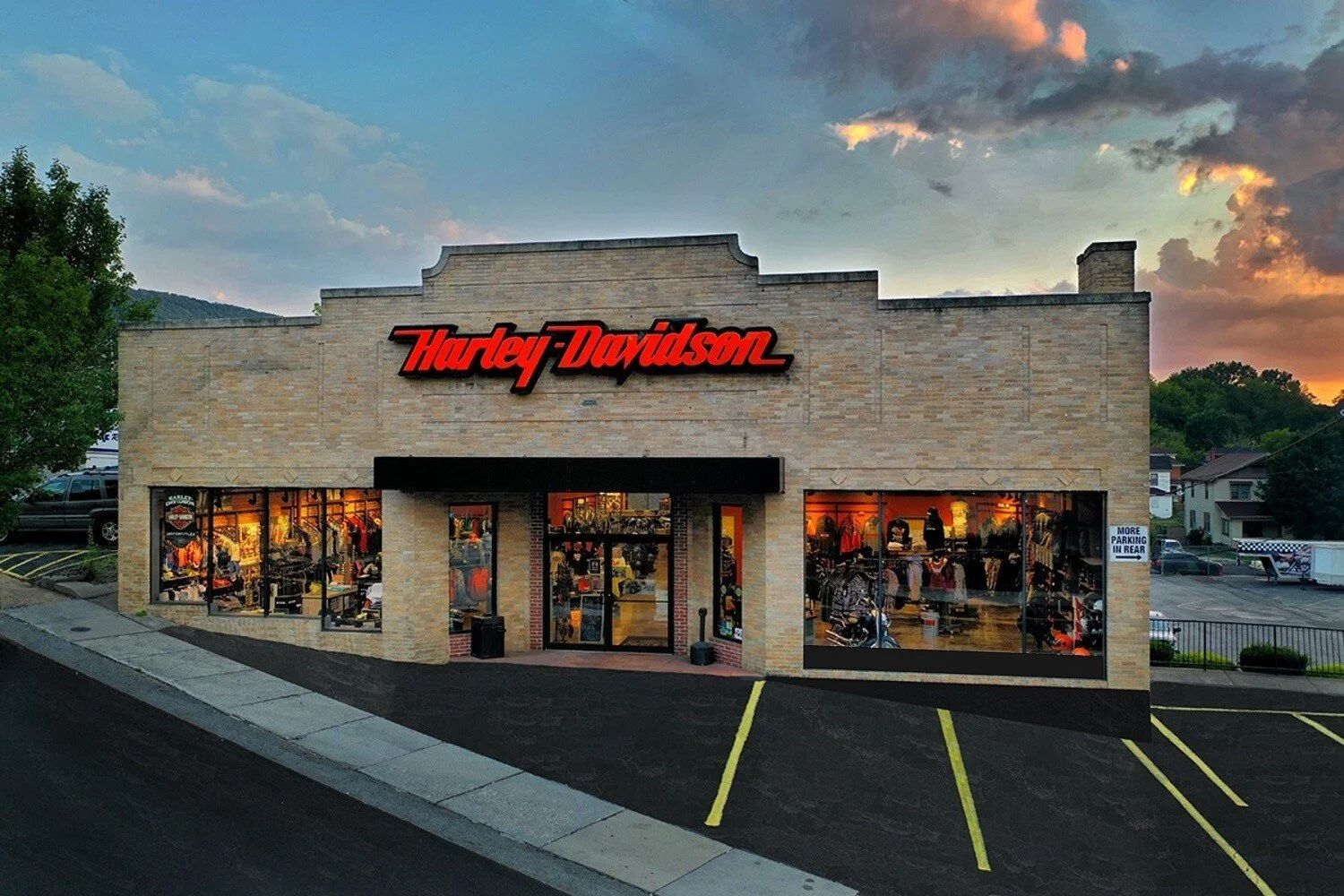 Harley Davidson store with a brick exterior, illuminated windows displaying motorcycle gear, and a red and black Harley Davidson sign, during sunset with a partly cloudy sky.