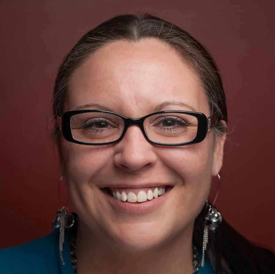 A woman with glasses smiling in front of a red background.
