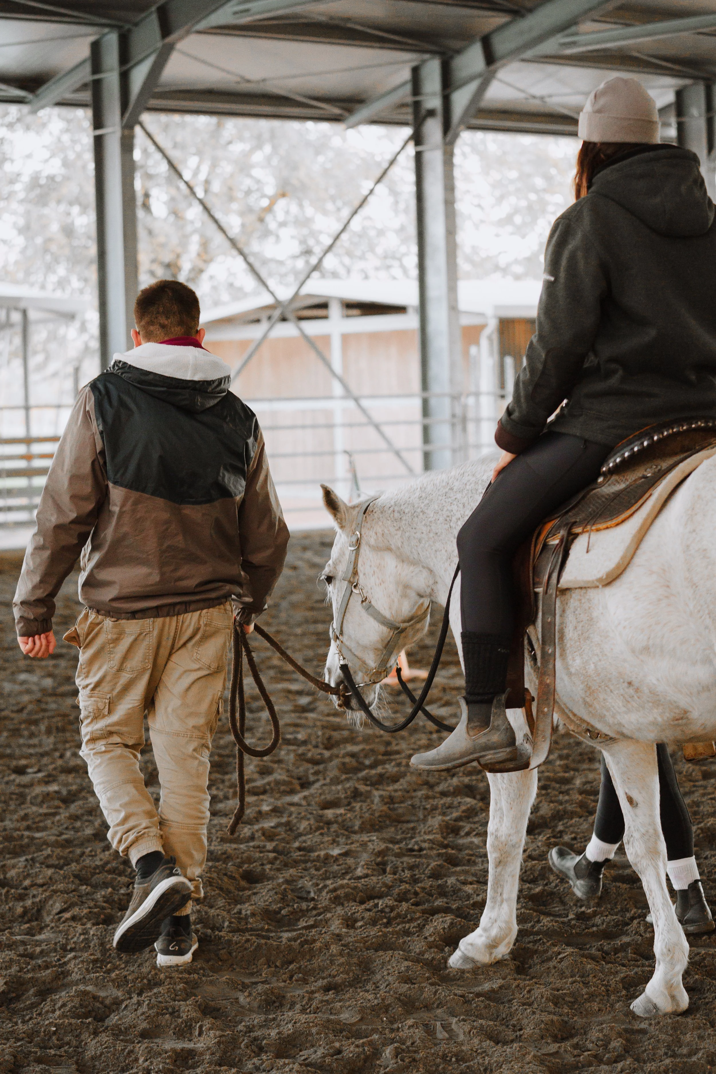 Due persone, una uomo e una donna, in un centro equestre. La donna è seduta su un cavallo bianco, mentre l'uomo la guida a piedi
