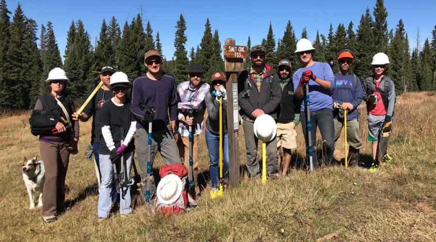 Group of twelve RTA volunteers at the Salt Creek trailhead. They are wearing hiking gear, hard hats, and holding trekking poles after finishing up a day of trail improvement.