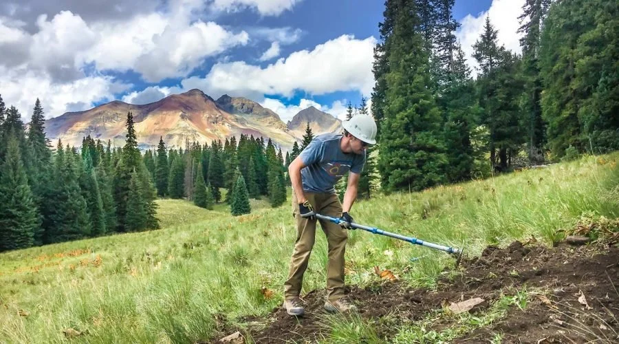 Person in a white helmet using a working to restore a section of mountain bike trail near Rico, Colorado.