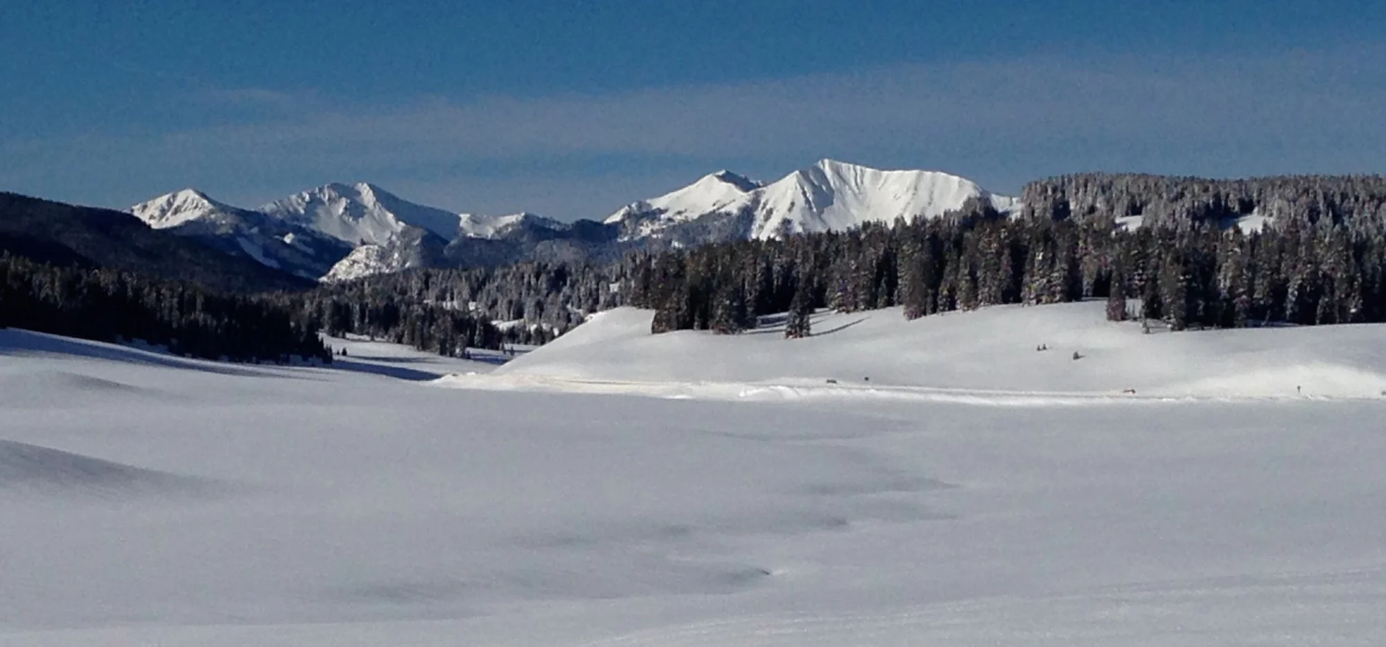 Snow-covered Rico with distant mountains, forested hills, and a clear blue sky.