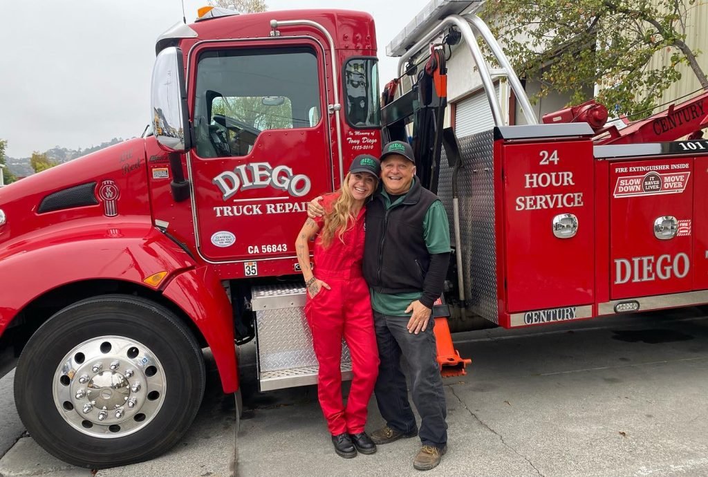 Doug Diego and daughter standing in front of Tow Truck with the words "DIEGO TRUCK REPAIR" and "24 HOUR SERVICE" on it.
