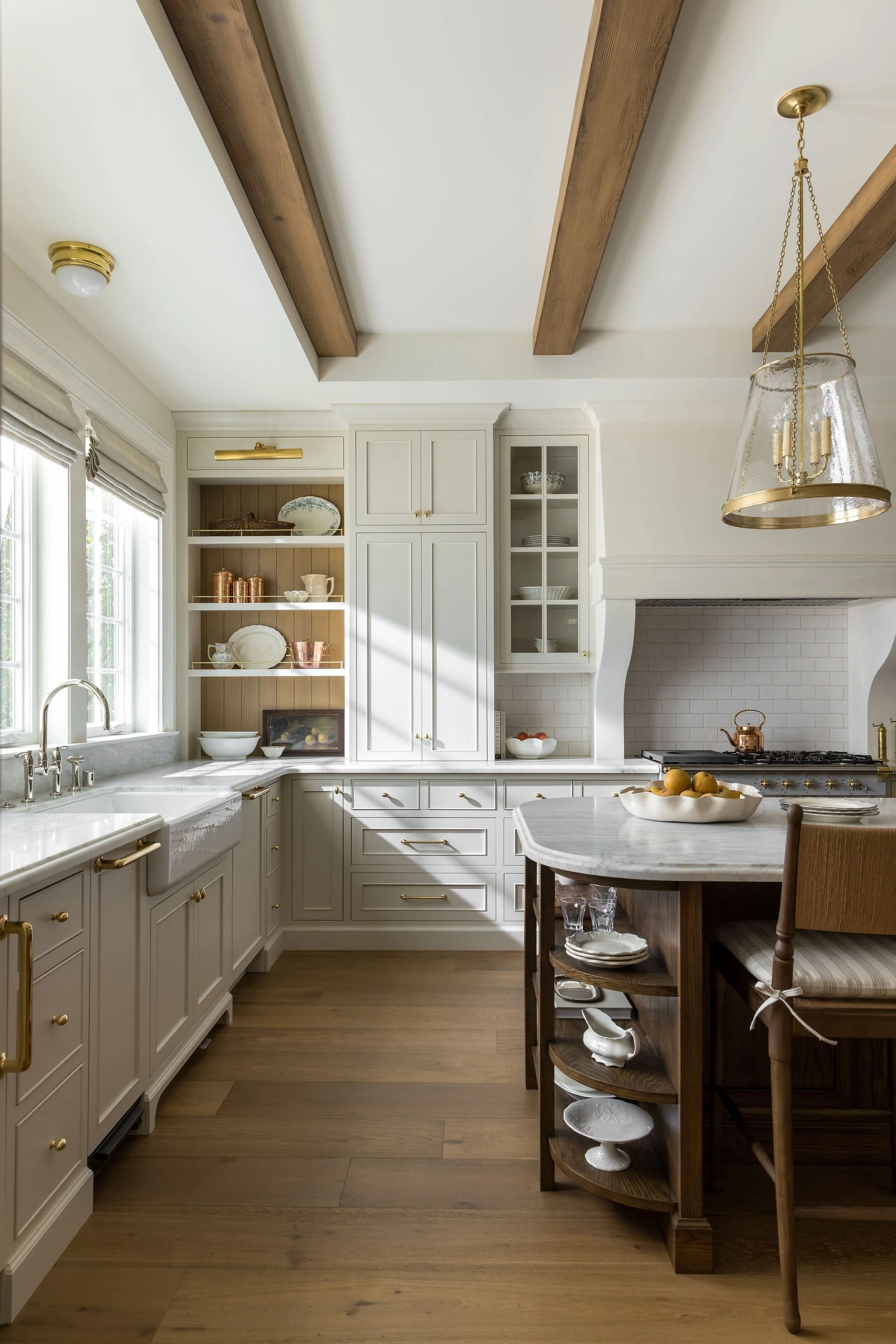 Bright kitchen with white cabinets, wooden beams on the ceiling, and a wooden island table with a bowl of lemons.
