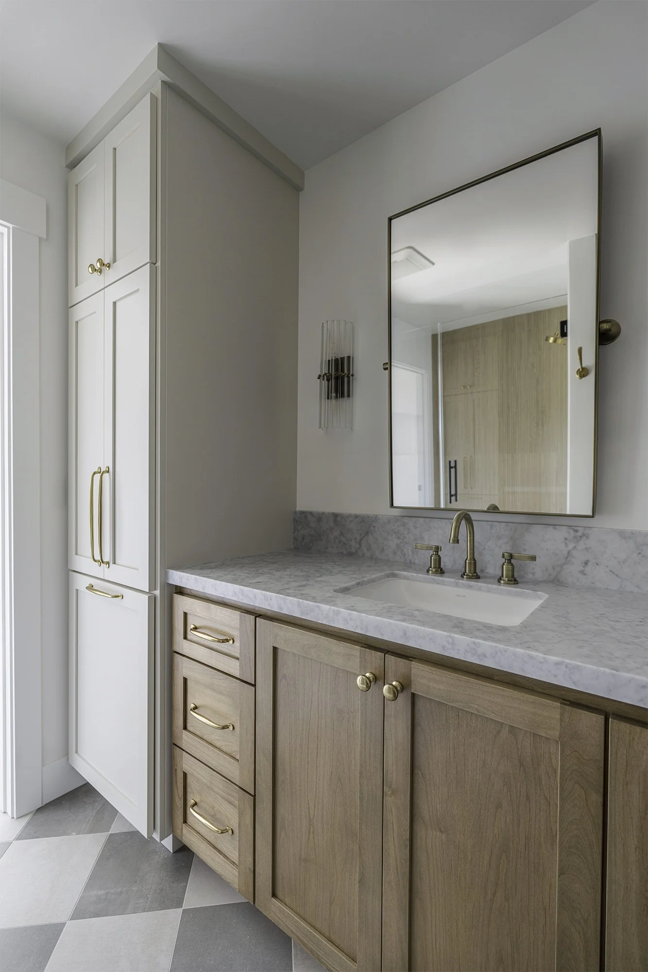 Bathroom vanity with marble countertop, gold fixtures, wooden cabinets, large mirror, and wall sconce