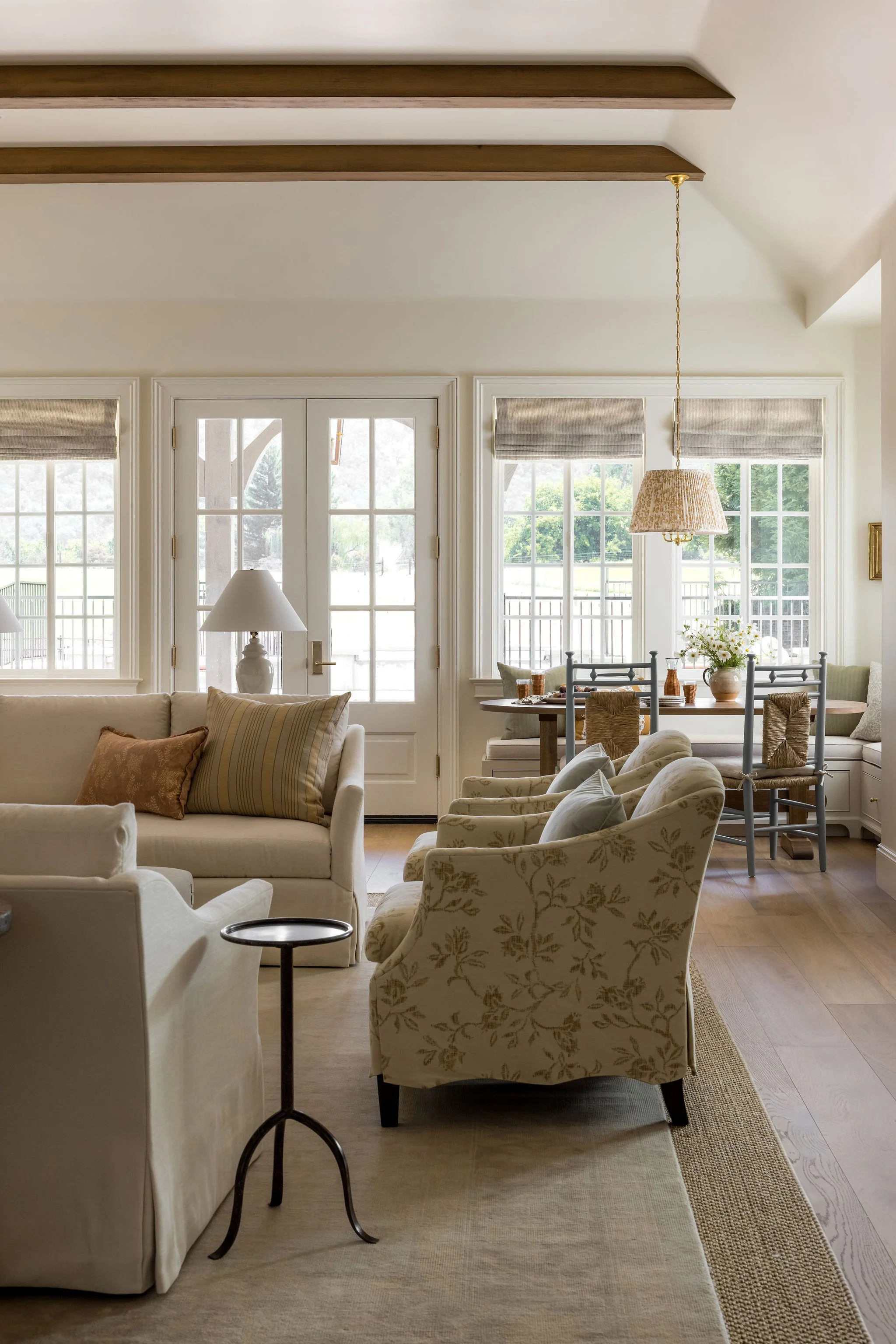Living room with white sofa and armchair, table with flowers, large windows, and chandelier.