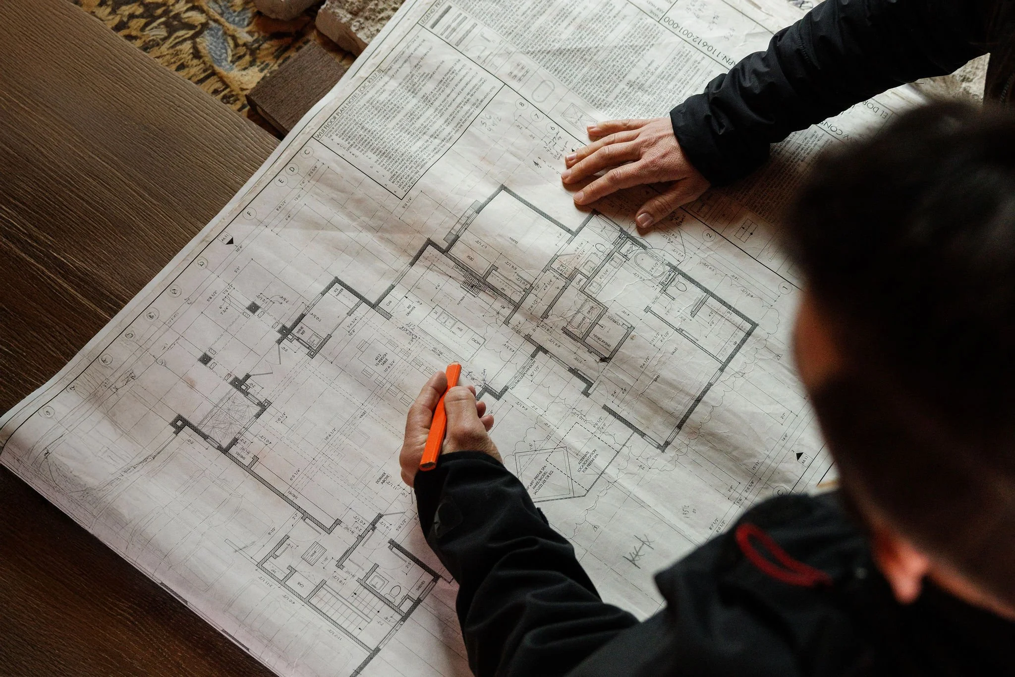 Two people reviewing architectural blueprints spread out on a wooden table.
