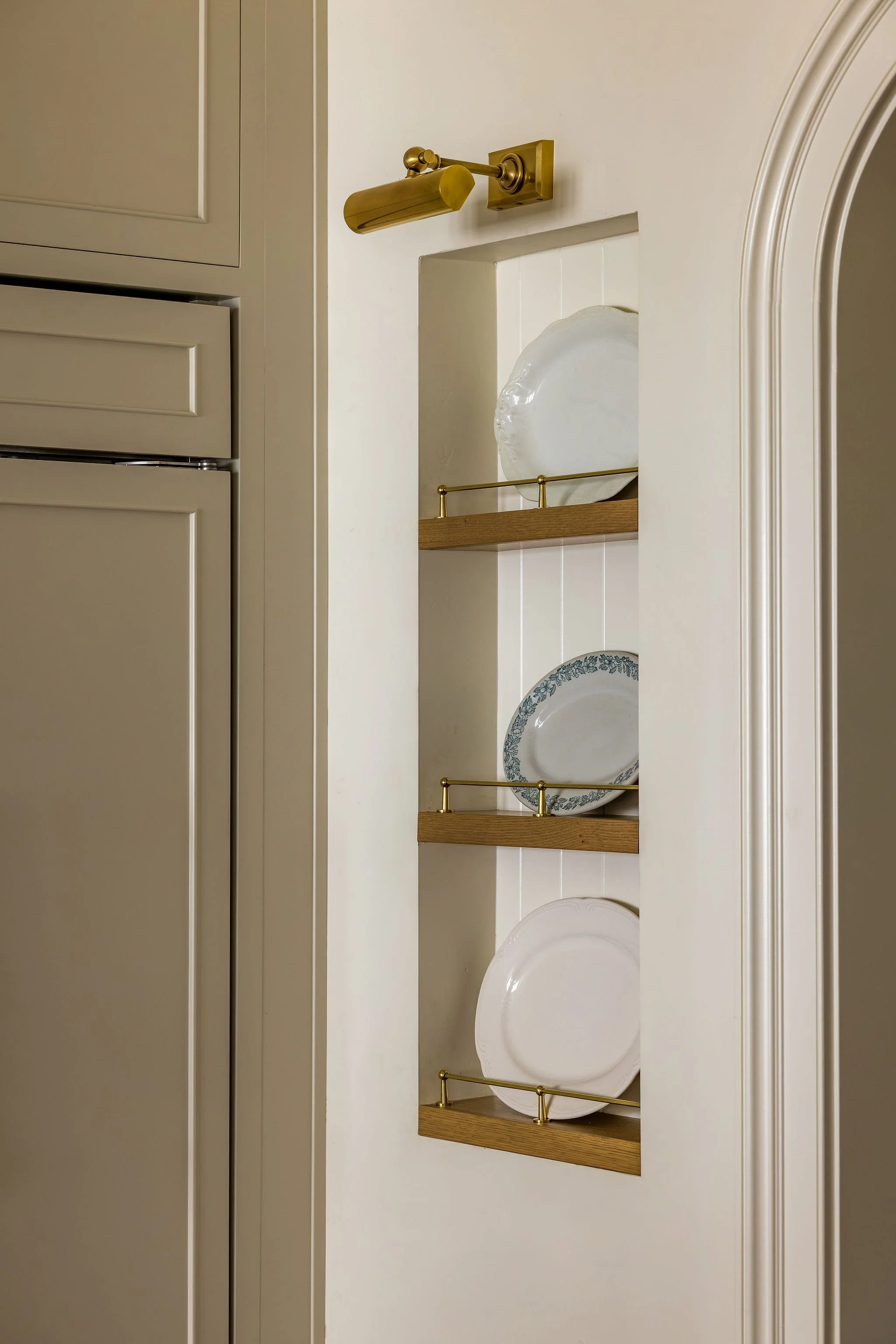 Open kitchen cabinet with plates and decorative shelf with a glass dish inside.