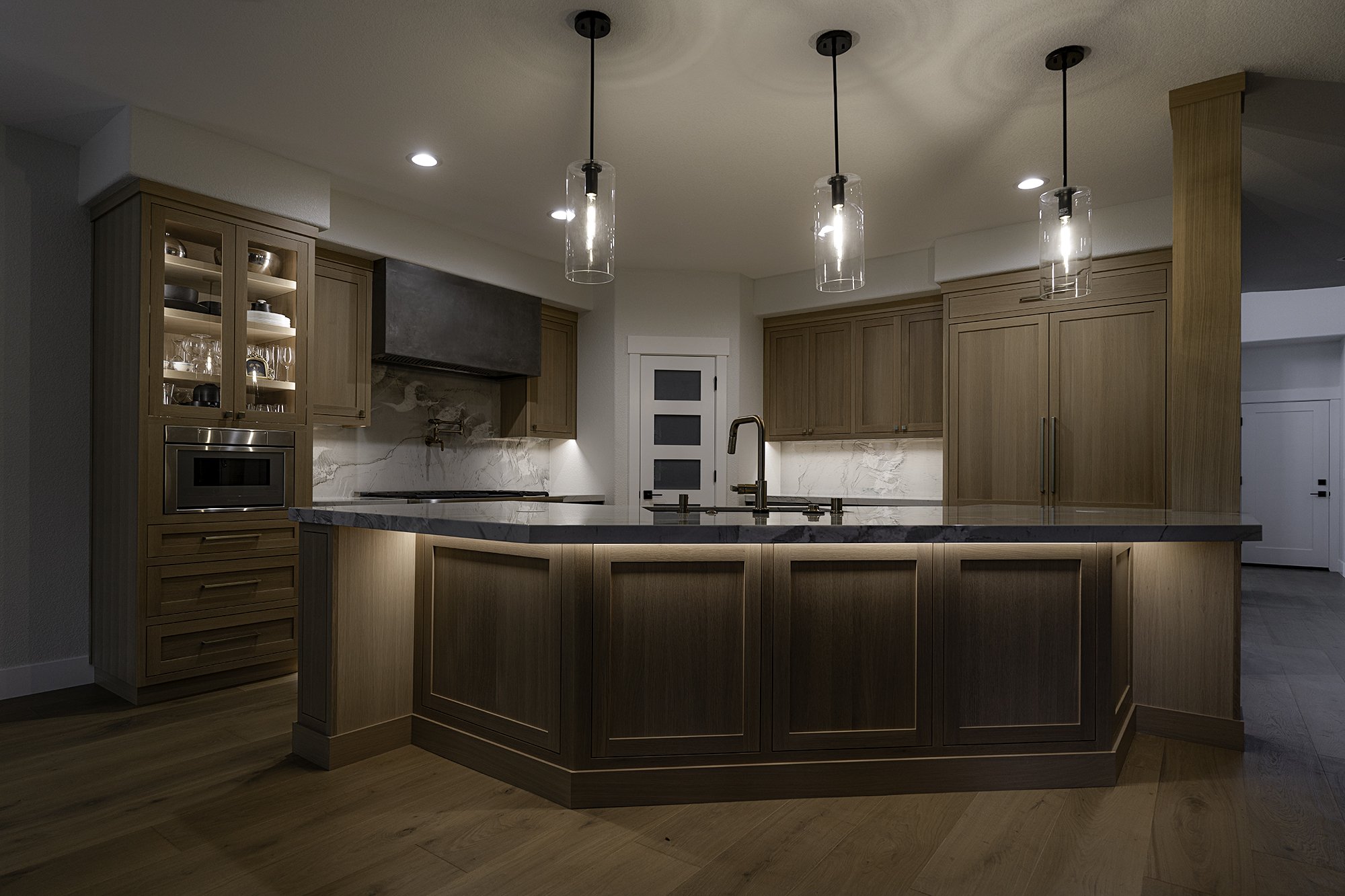 Modern kitchen with wooden cabinets, marble countertops, a centrally located island, hanging pendant lights, and built-in appliances.
